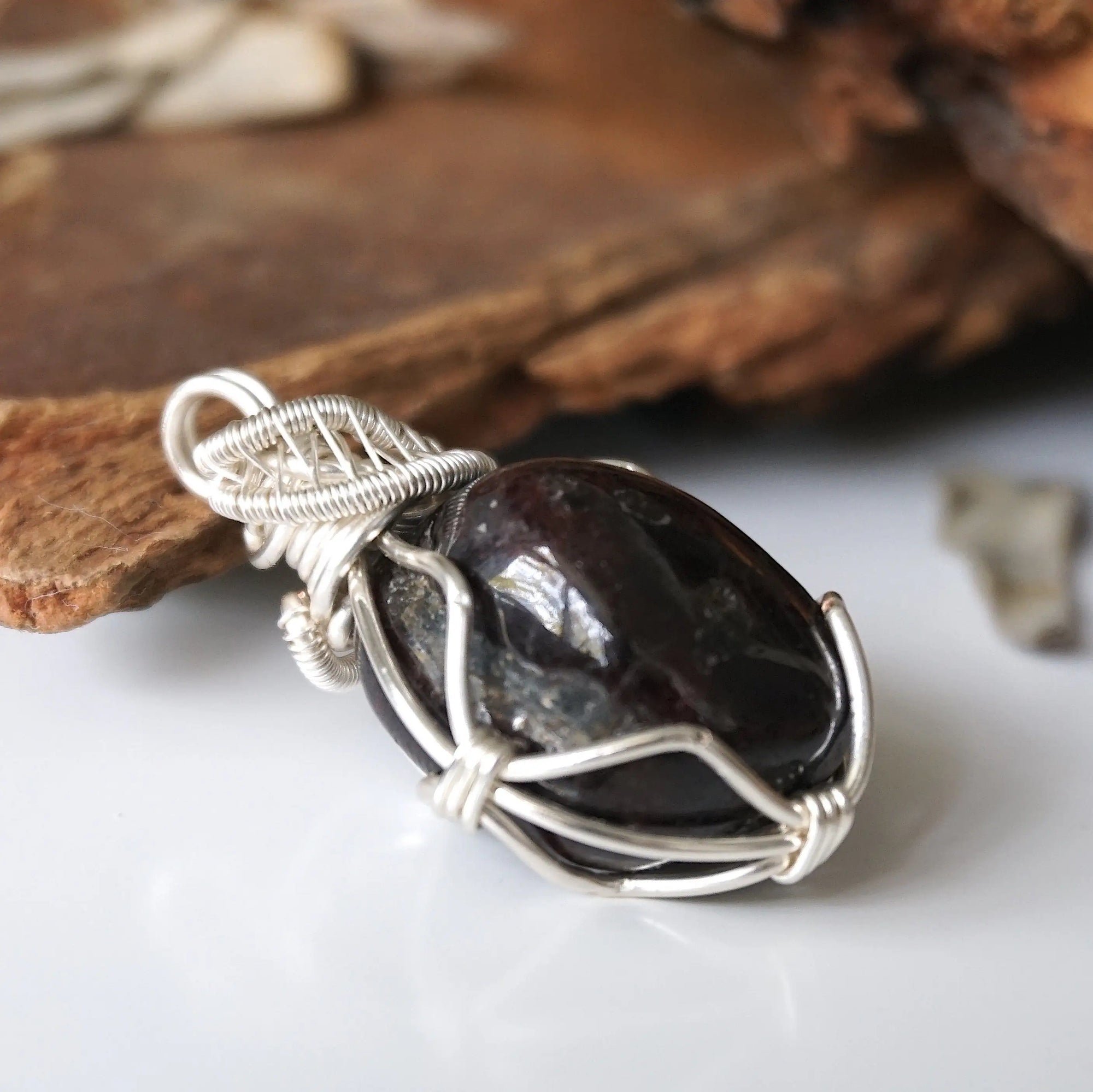 Side angle of wire wrapped garnet pendant showing detailed silver plated copper wrap and raw crystal texture