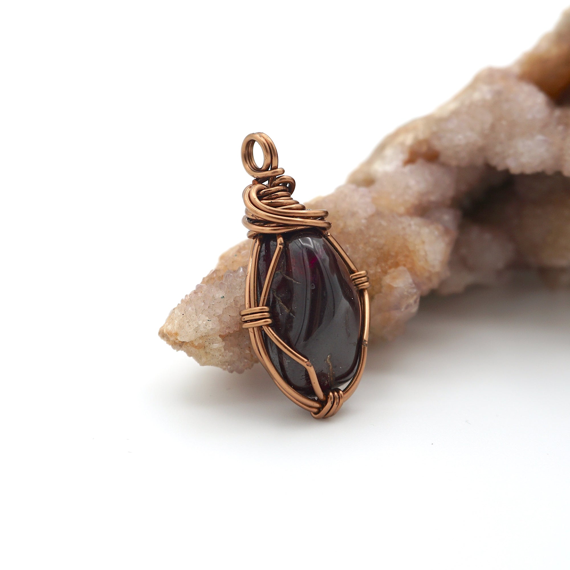 Side angle view of natural garnet pendant with simple antique bronze copper wire wrapping
