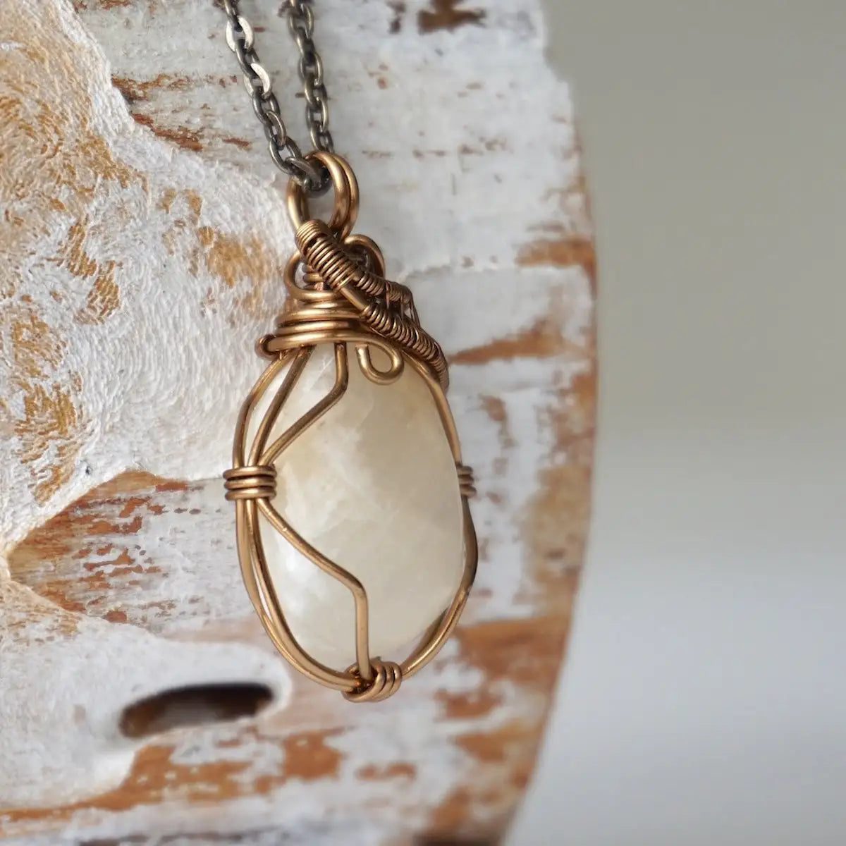 Right angle close-up of polished-raw moonstone pendant with detailed artisan antique bronze wire wrapping on cable chain.
