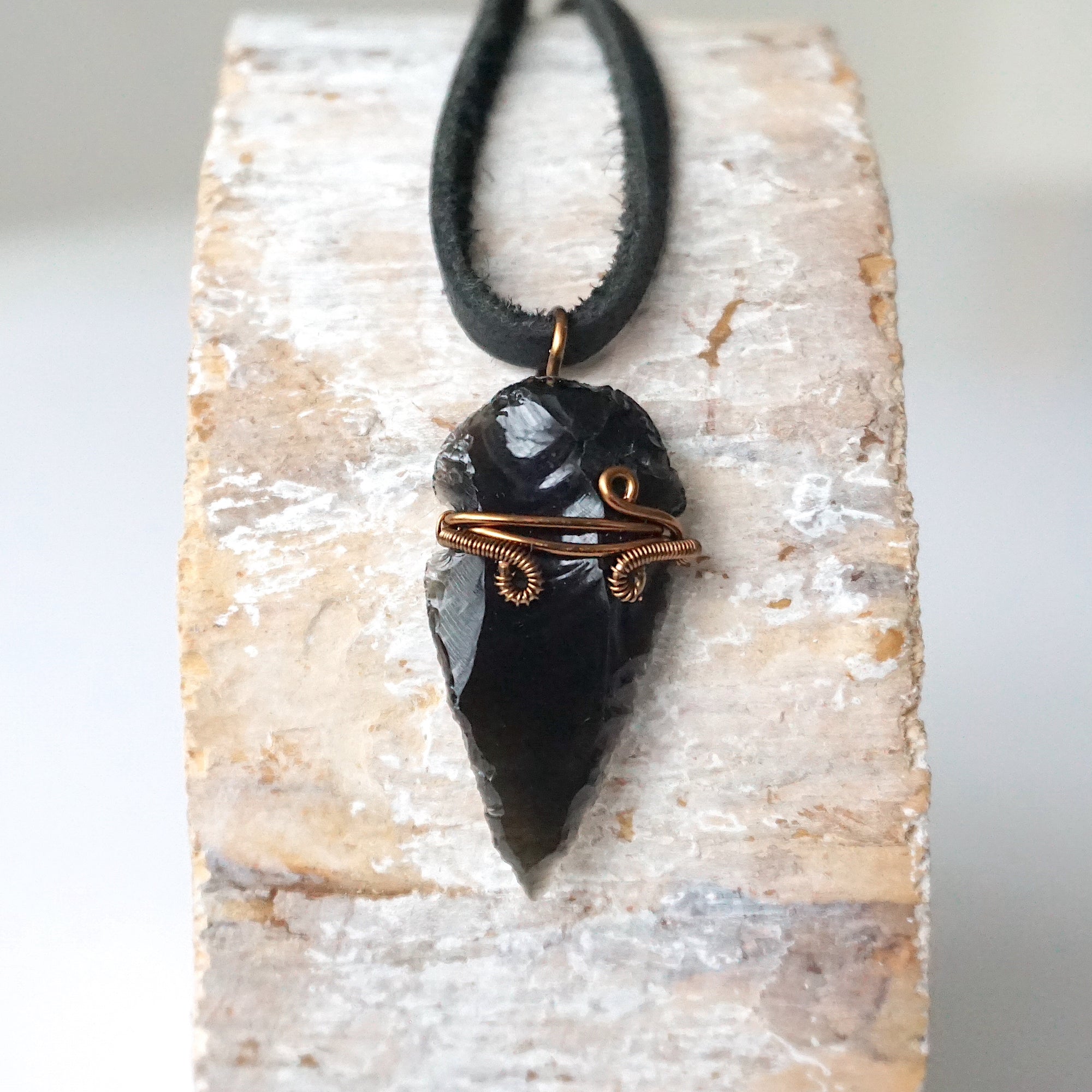 Detailed front view of men’s black obsidian arrowhead necklace on black leather cord, antique bronze copper wire wrap, by Designs by Nature Gems.