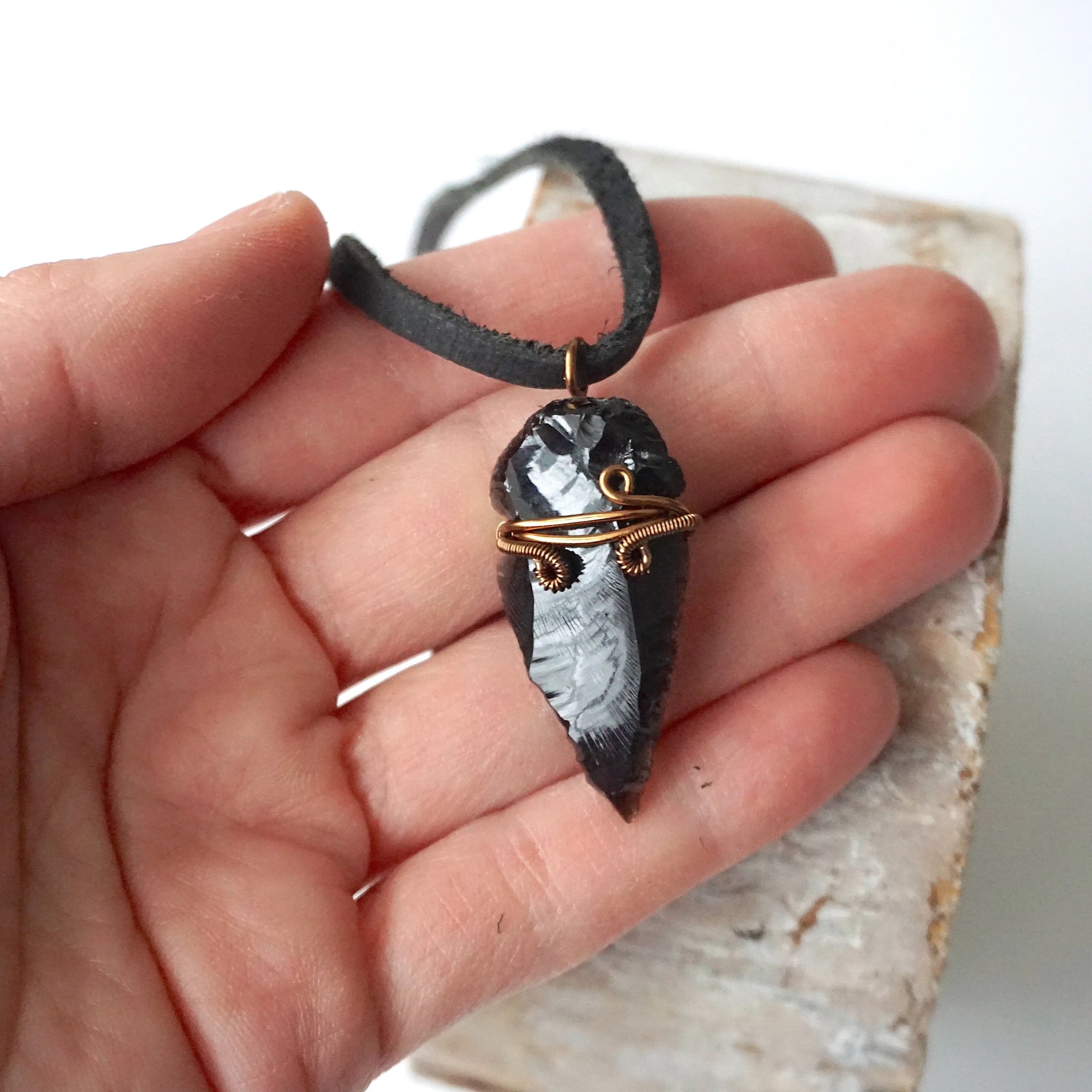 Black obsidian arrowhead necklace for men with antique bronze copper wire wrap, shown in hand for size reference, by Designs by Nature Gems.