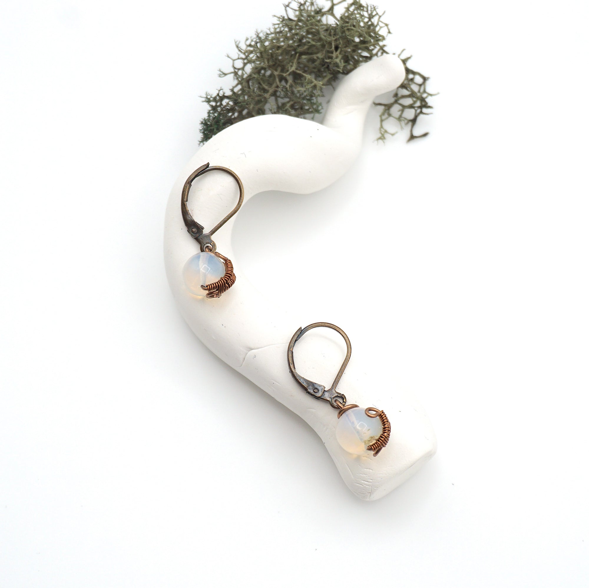 Bird’s eye view of opal drop earrings laying flat on a display, showing detailed wire wrapping and gemstone color.