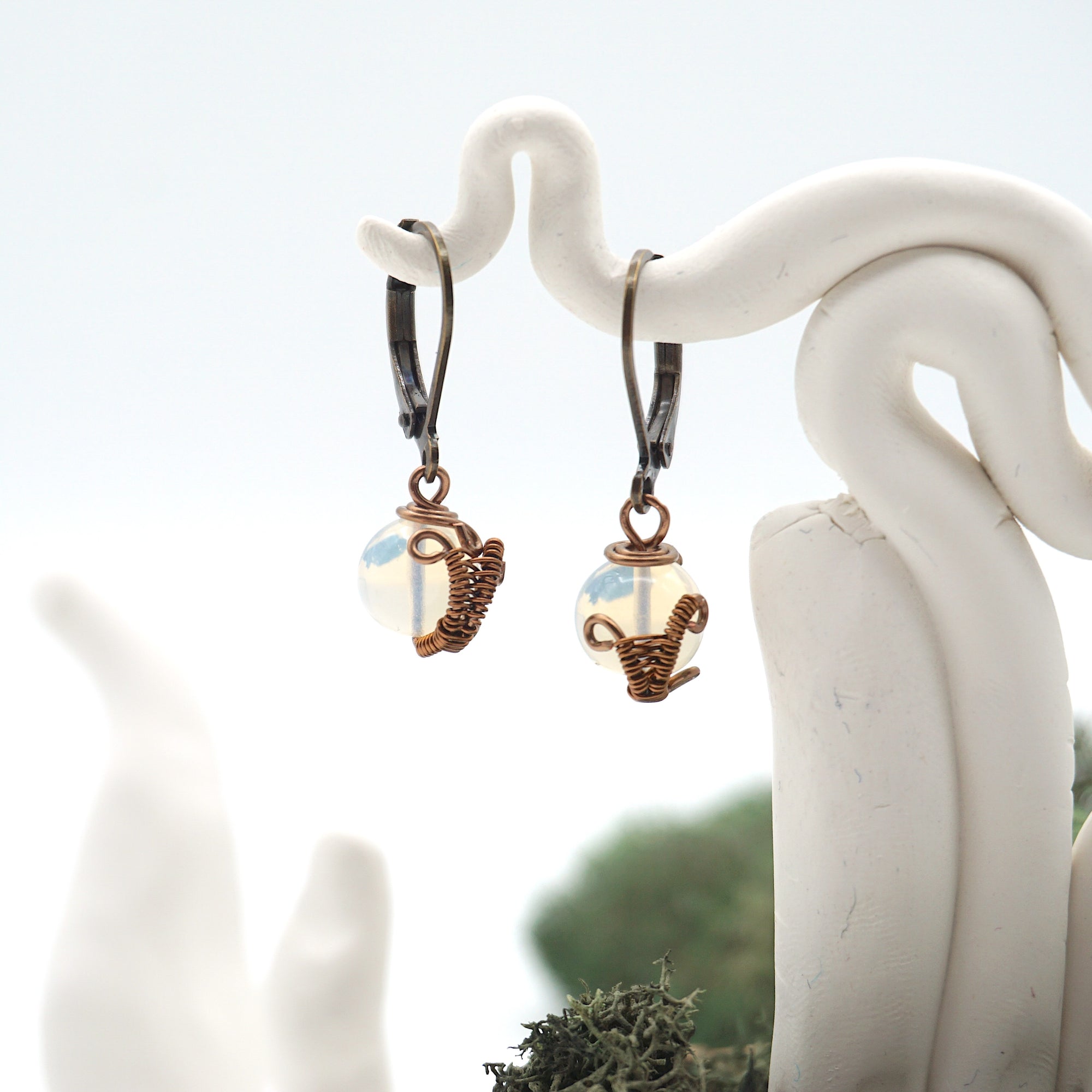 Close-up of handcrafted opal drop earrings with antique bronze copper wire wrapping.