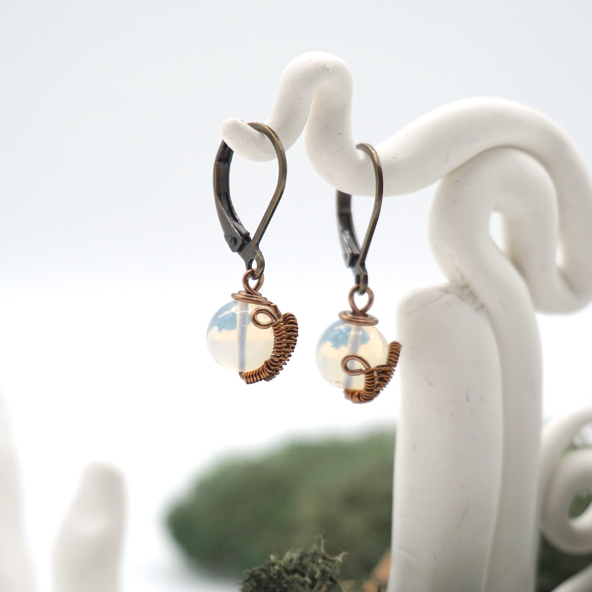 Side angle of opal drop earrings on a display stand, highlighting antique bronze copper wire wrapping.