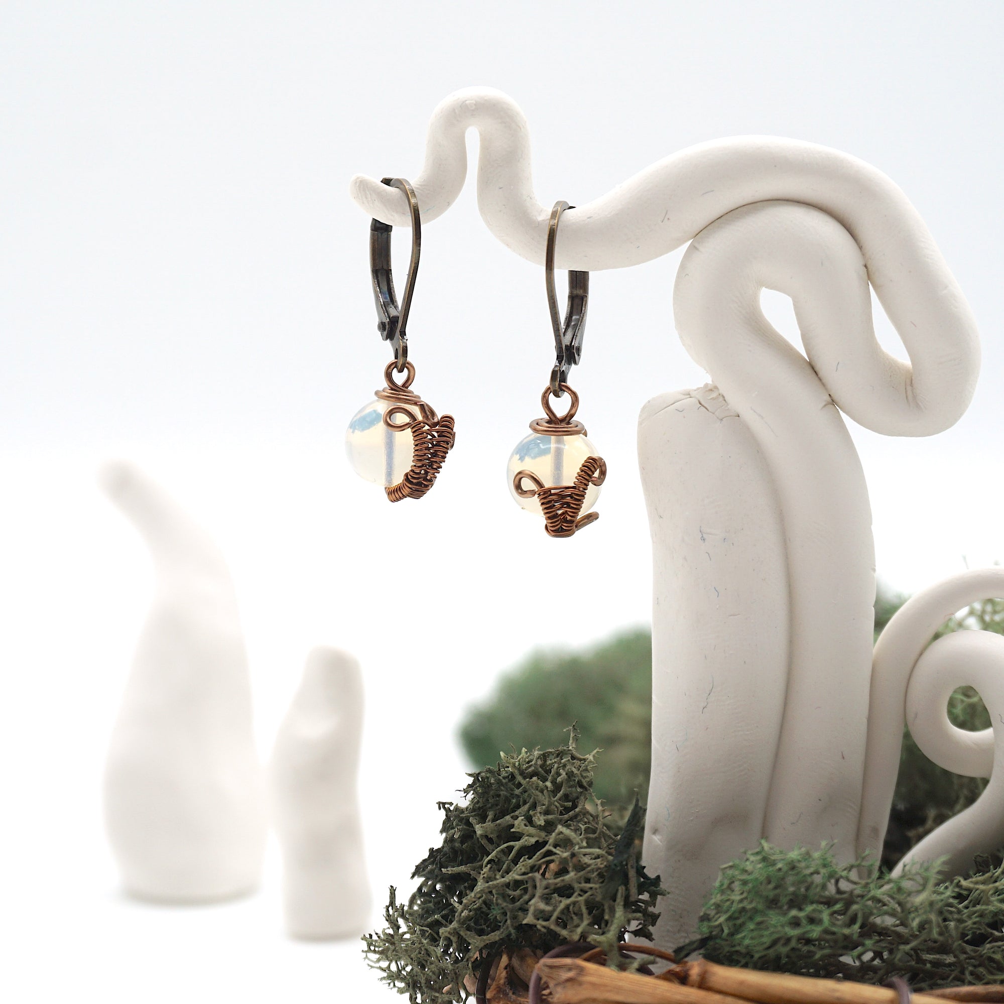 Front angle of opal drop earrings hanging on a jewelry display, wire-wrapped design.