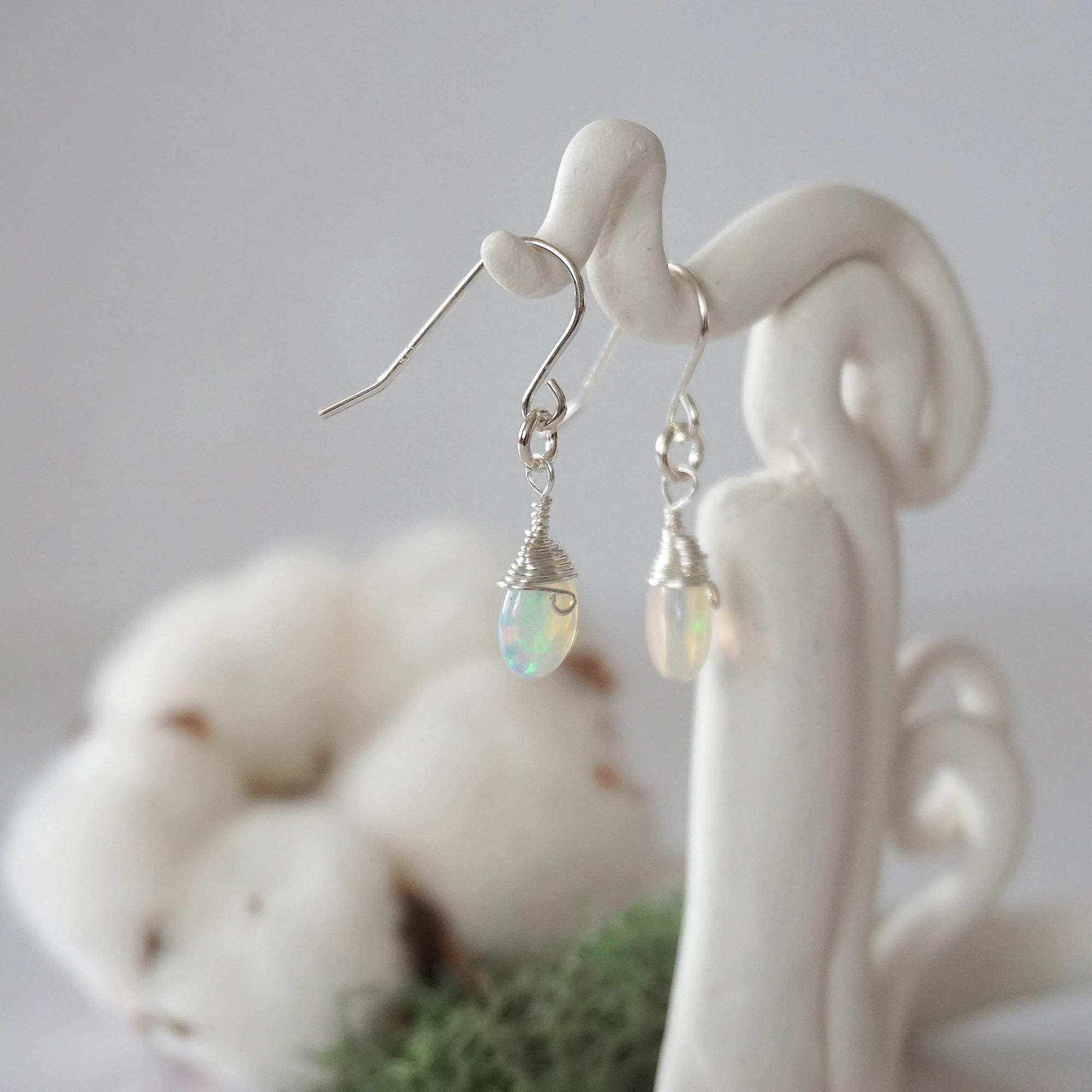 Side view of opal sterling silver drop earrings showing wire wrapped natural faceted opal, artisan craftsmanship, on a display – Designs by Nature Gems