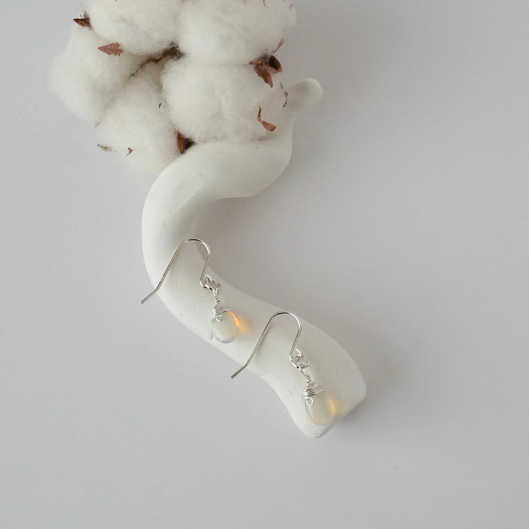 Opal sterling silver drop earrings with faceted natural opal stones and wire wrapping, laying flat on a display – Designs by Nature Gems