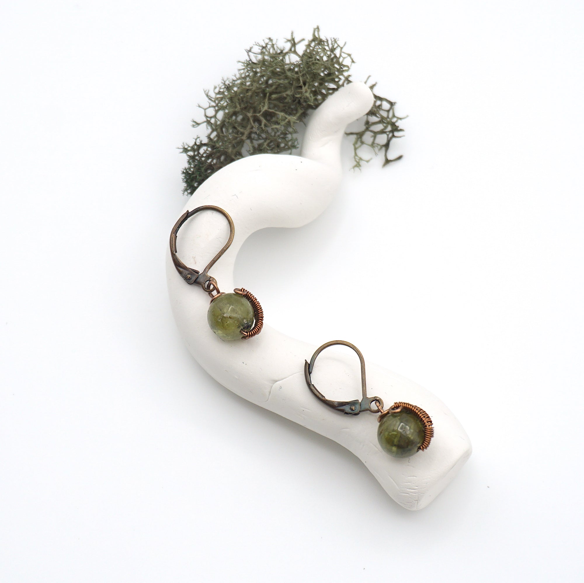 Bird’s eye view of peridot drop earrings laying flat on a display, showing detailed wire wrapping and gemstone color.