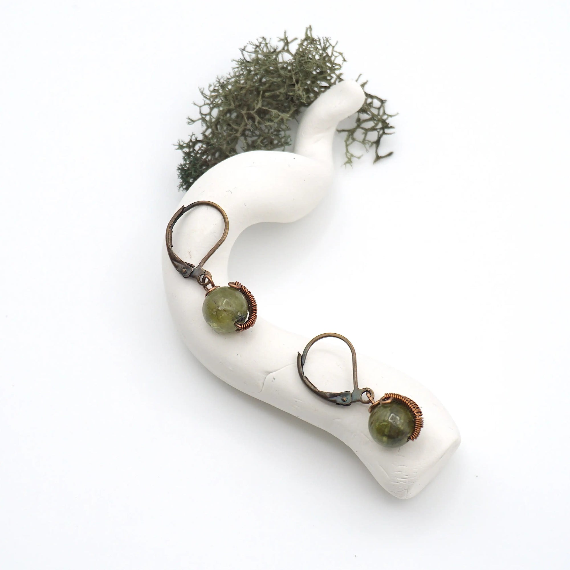 Bird’s eye view of peridot drop earrings laying flat on a display, showing detailed wire wrapping and gemstone color.