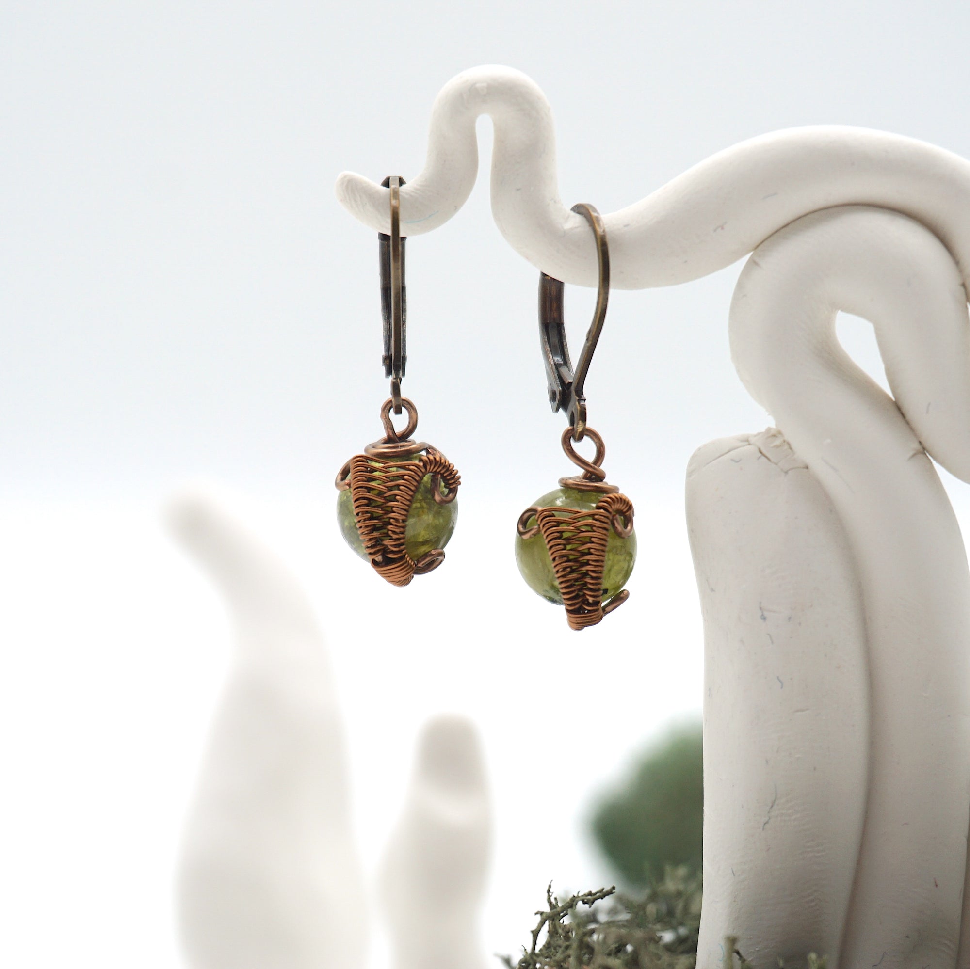 Close-up of handcrafted peridot drop earrings with antique bronze copper wire wrapping.
