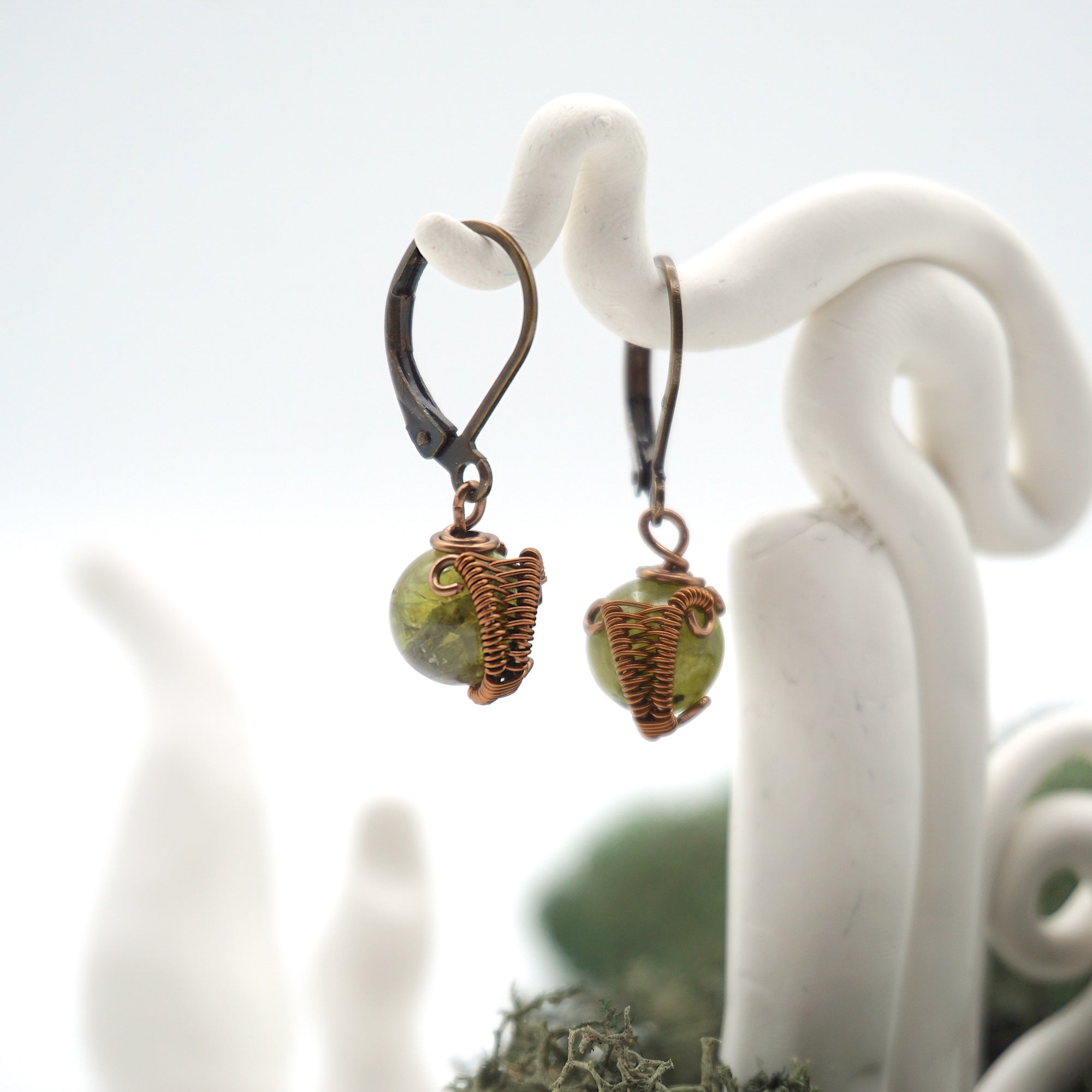 Side angle of peridot drop earrings on a display stand, highlighting antique bronze copper wire wrapping.