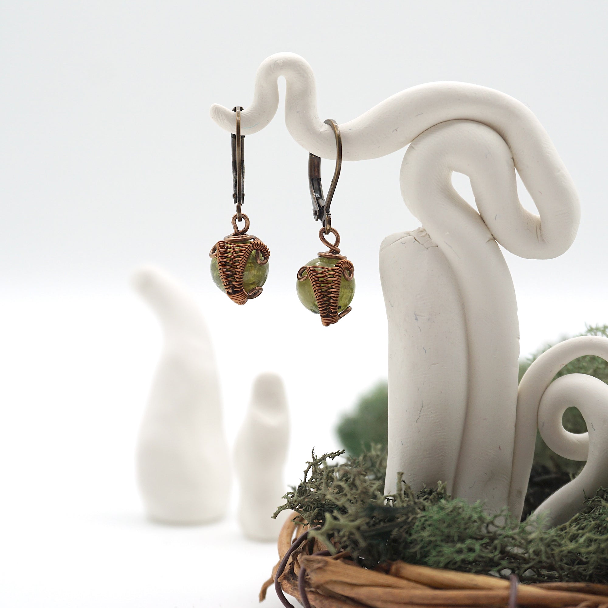 Front angle of peridot drop earrings hanging on a jewelry display, wire-wrapped design.