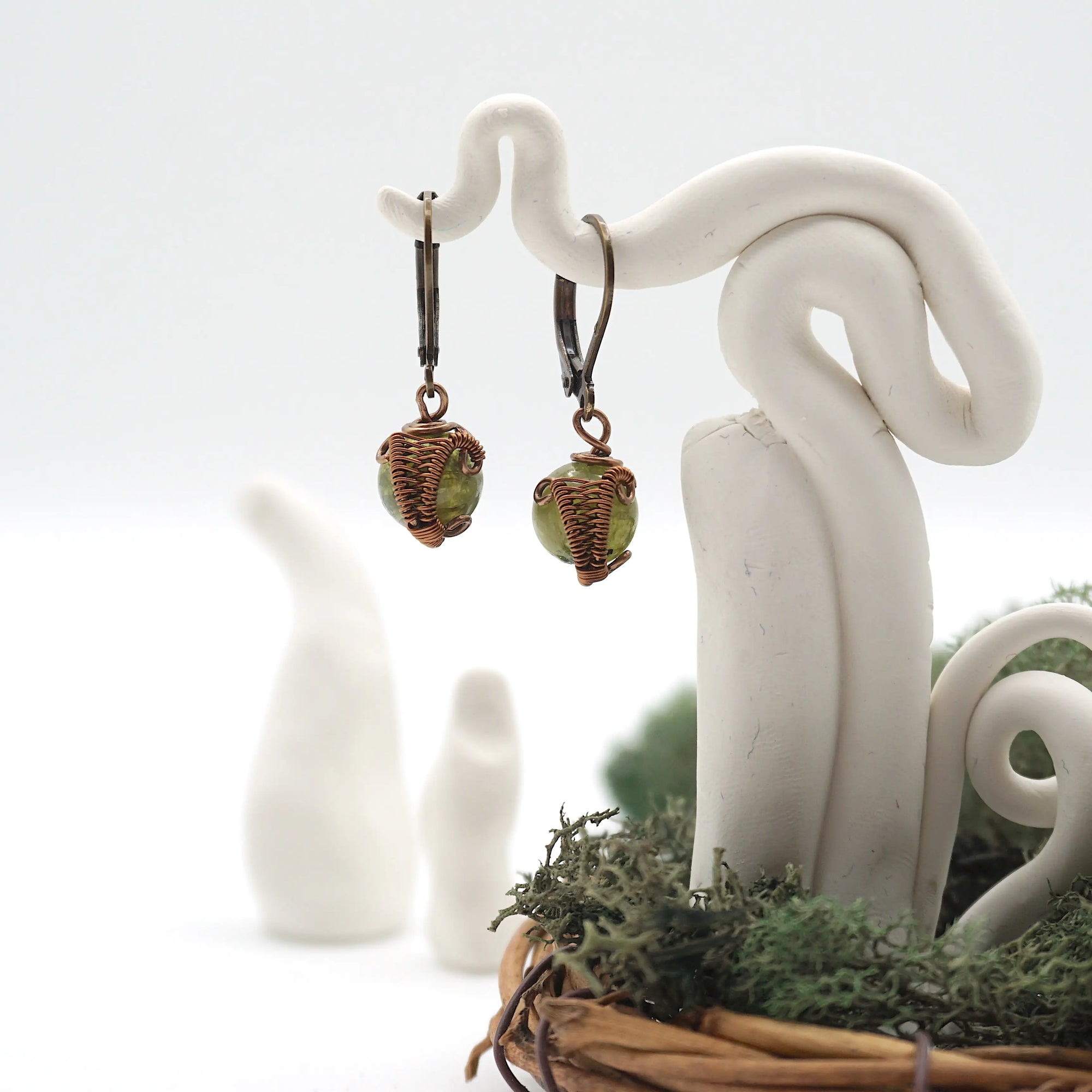Front angle of peridot drop earrings hanging on a jewelry display, wire-wrapped design.