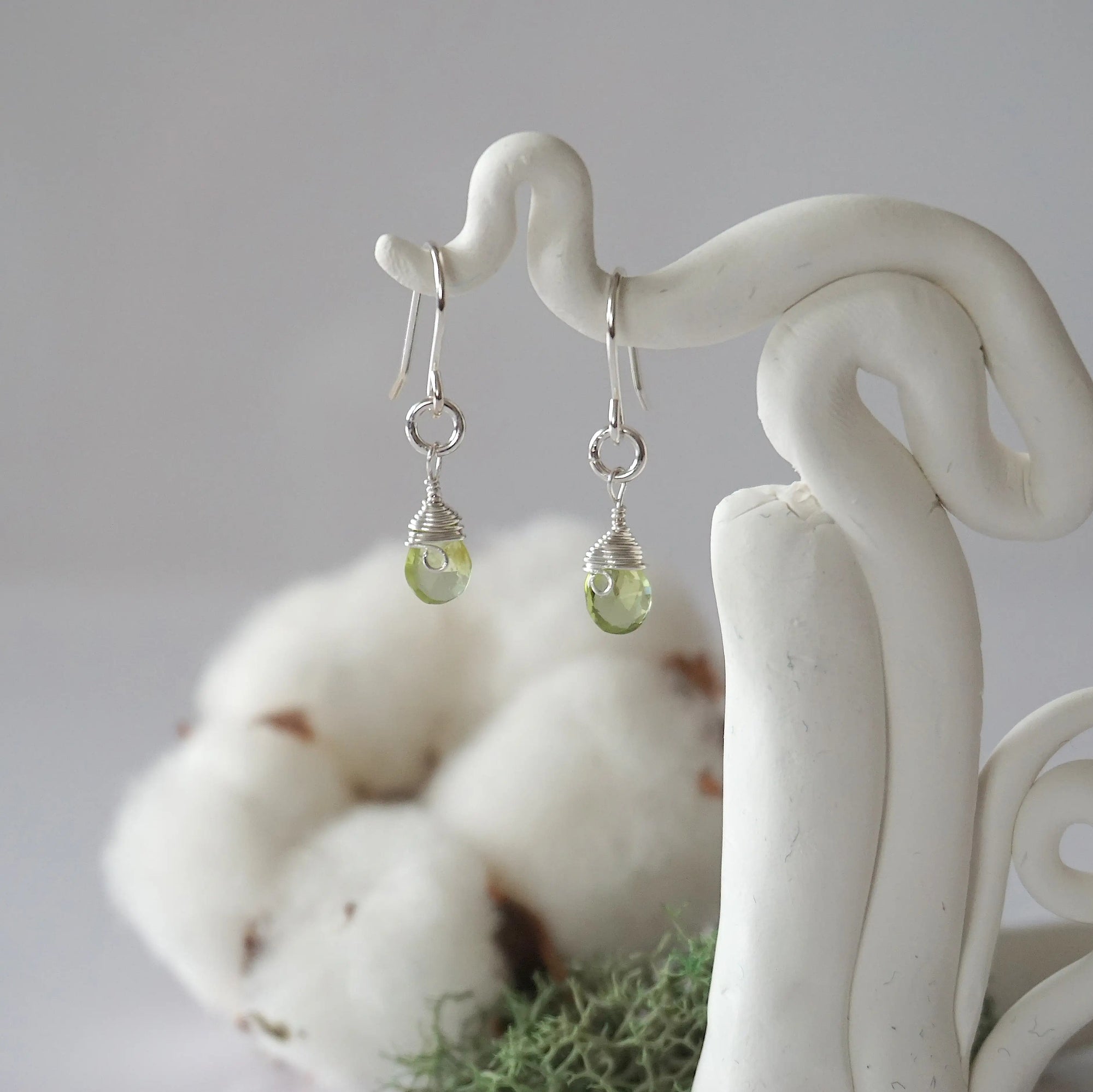 Detailed front view of handcrafted peridot sterling silver drop earrings with natural faceted peridot, artisan wire wrapping, hanging from a display – Designs by Nature Gems