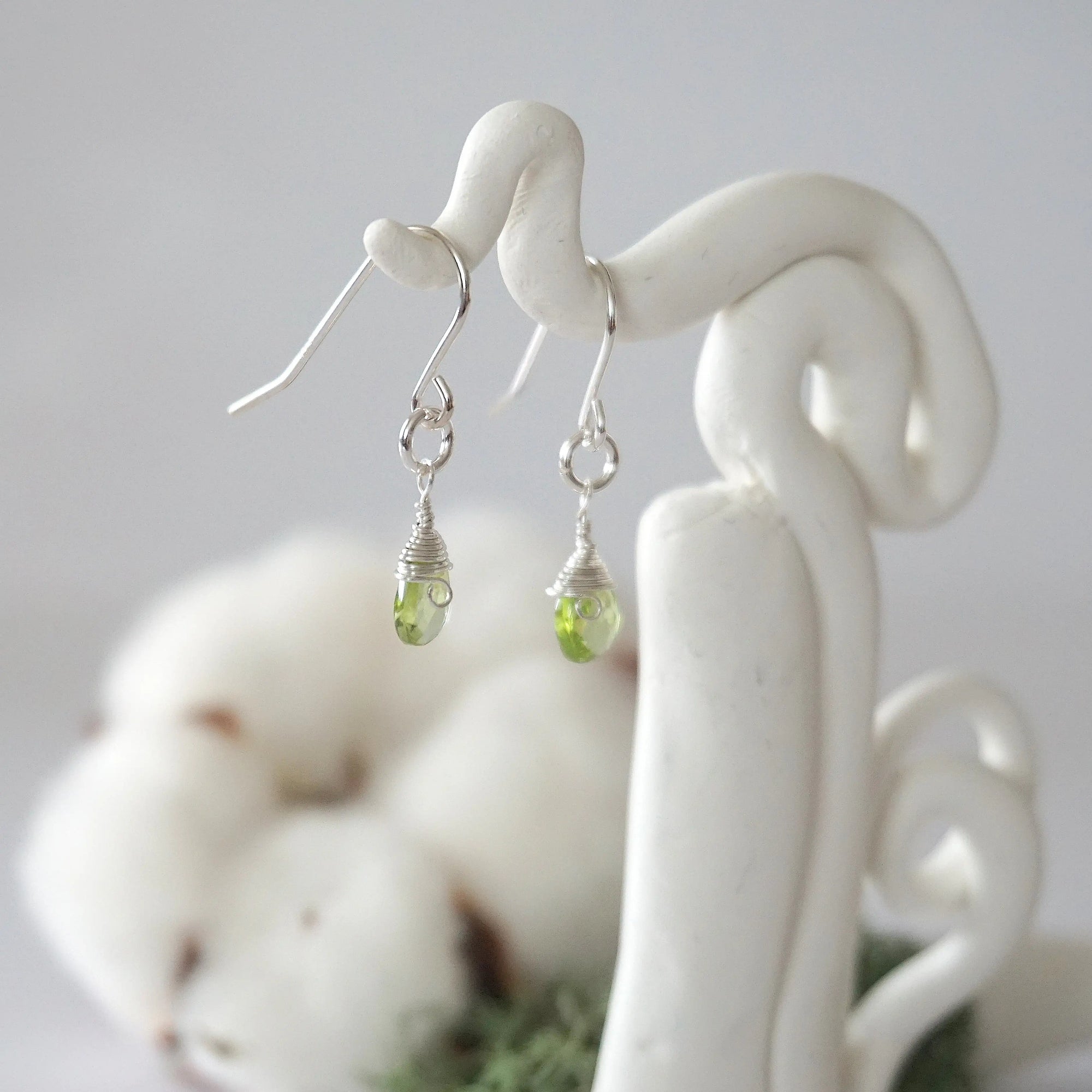 Side view of peridot sterling silver drop earrings showing wire wrapped natural faceted peridot, artisan craftsmanship, on a display – Designs by Nature Gems