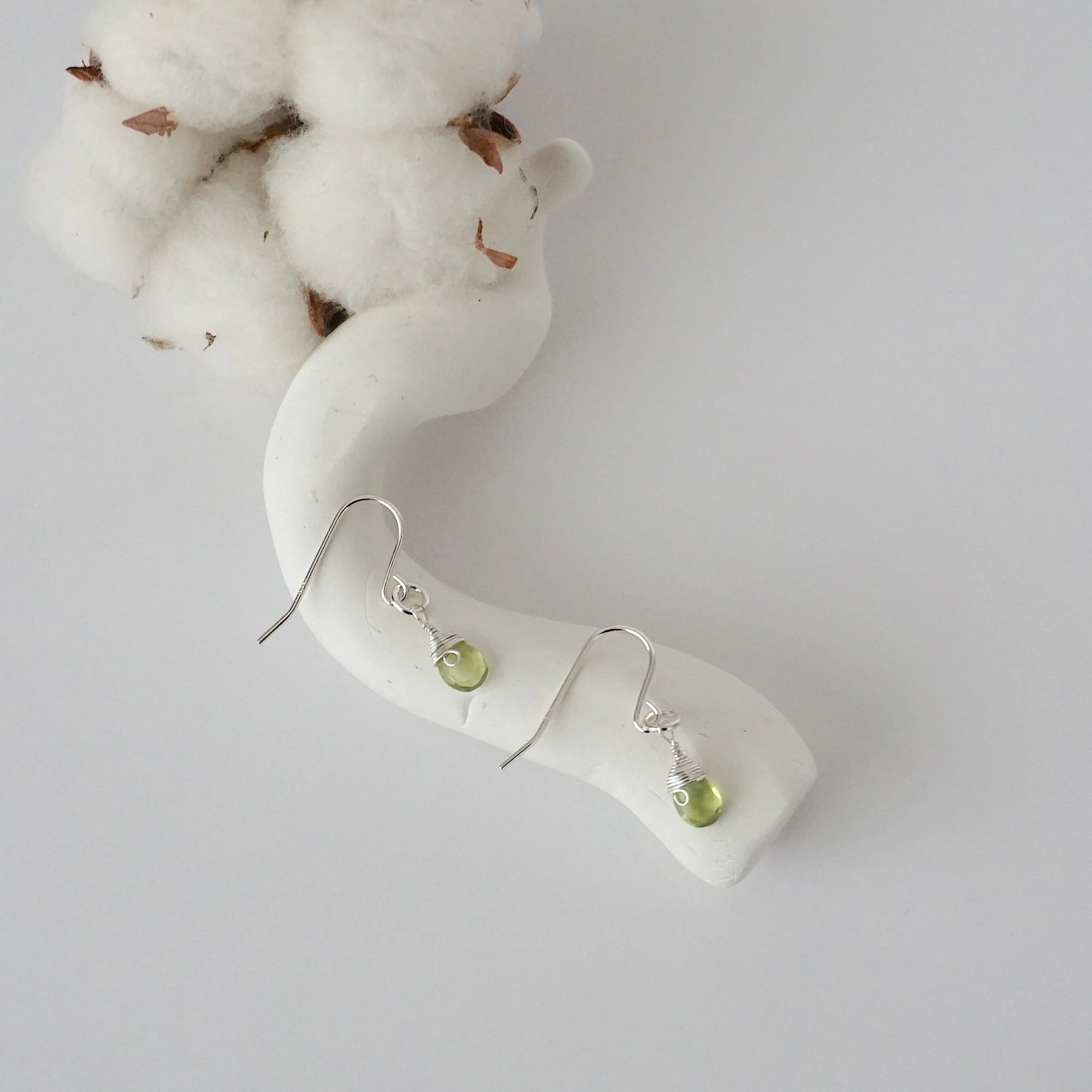 Peridot sterling silver drop earrings with faceted natural peridot stones and wire wrapping, laying flat on a display – Designs by Nature Gems