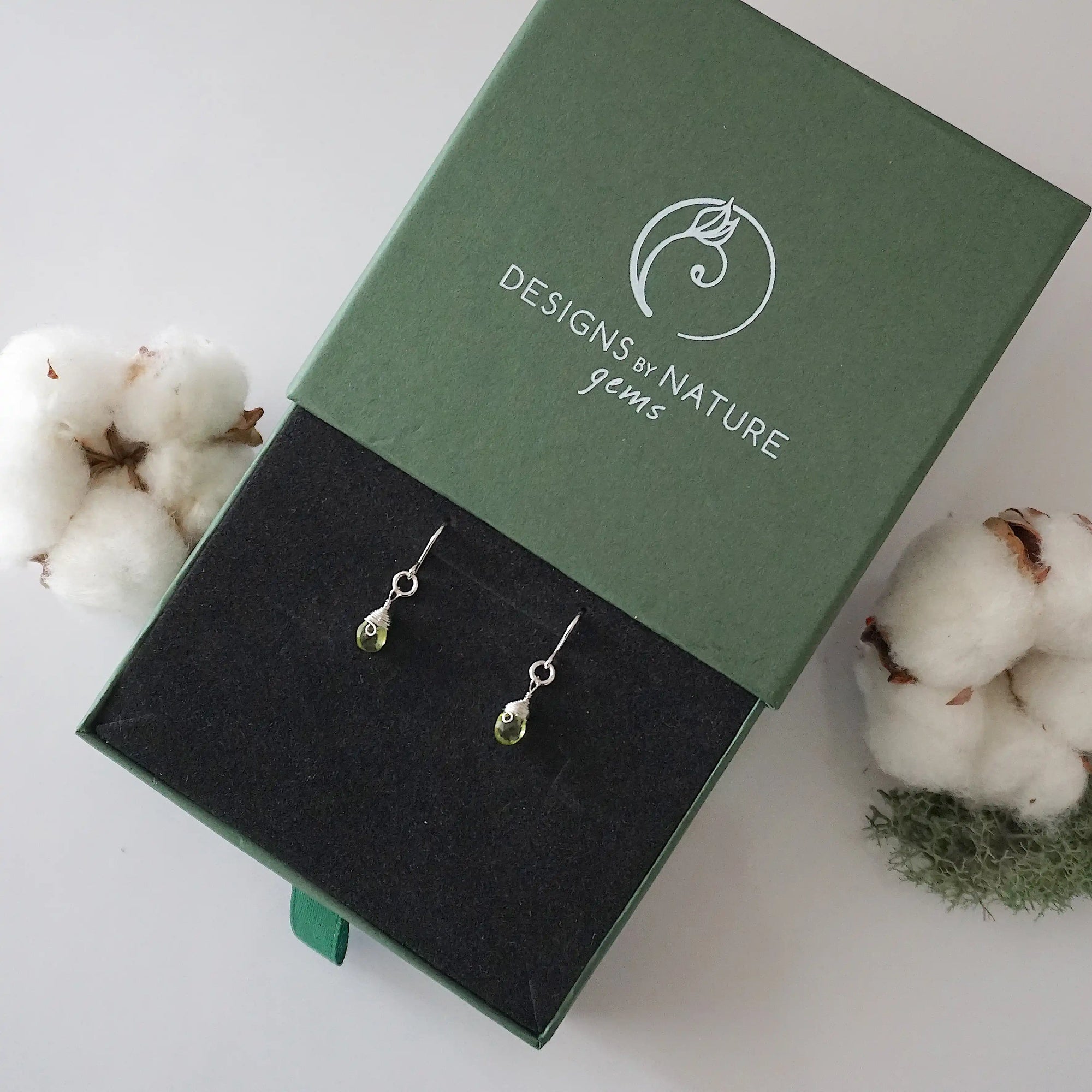 Peridot sterling silver drop earrings in branded Designs by Nature Gems jewelry box, showcasing handcrafted faceted peridot and sterling silver wire wrapping