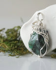 Left angle view of emerald necklace for women with natural polished-raw emerald and detailed sterling silver wire wrapping
