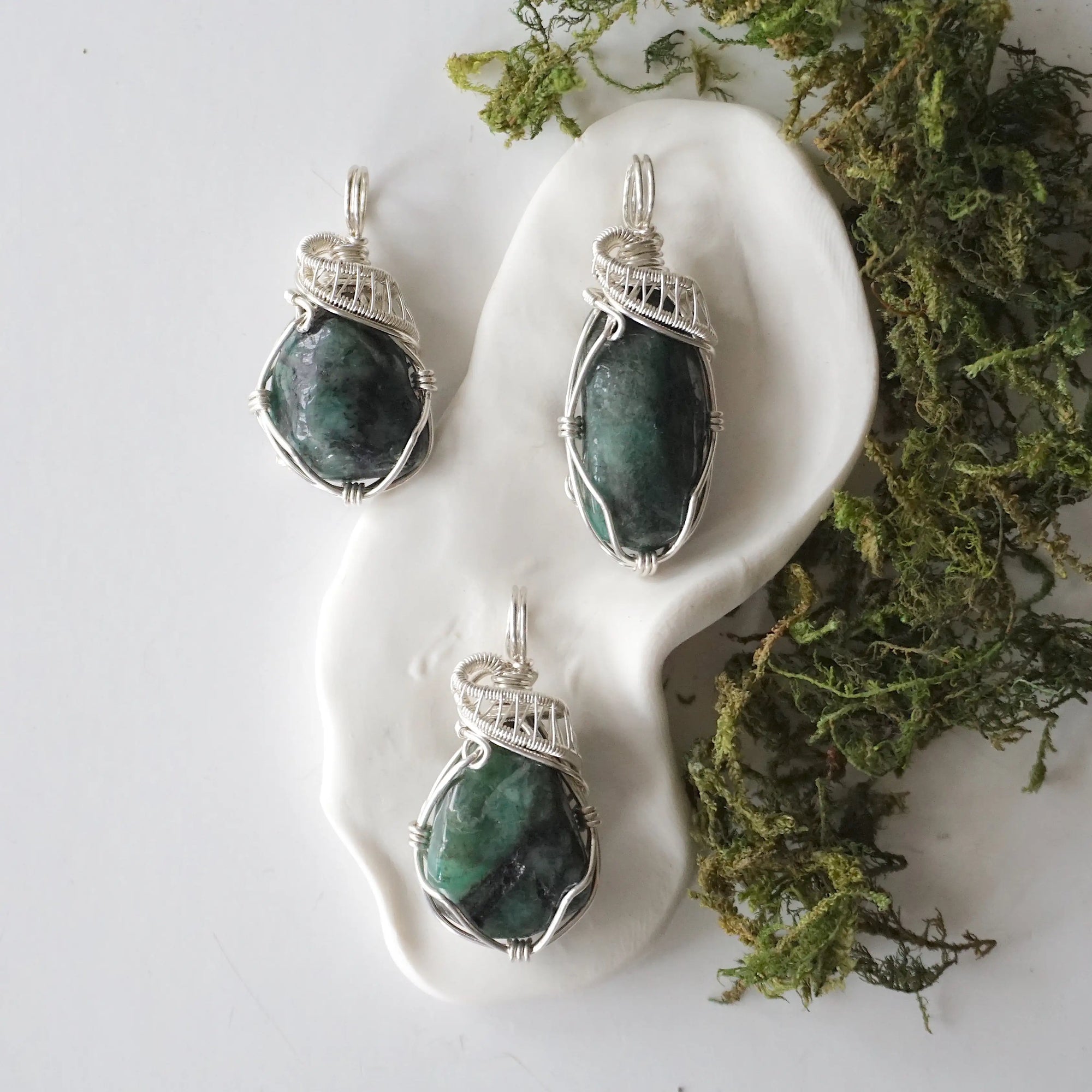 Three polished raw emerald pendants for women showing natural variation in emerald size, shape, and green colour in sterling silver wire wrapping