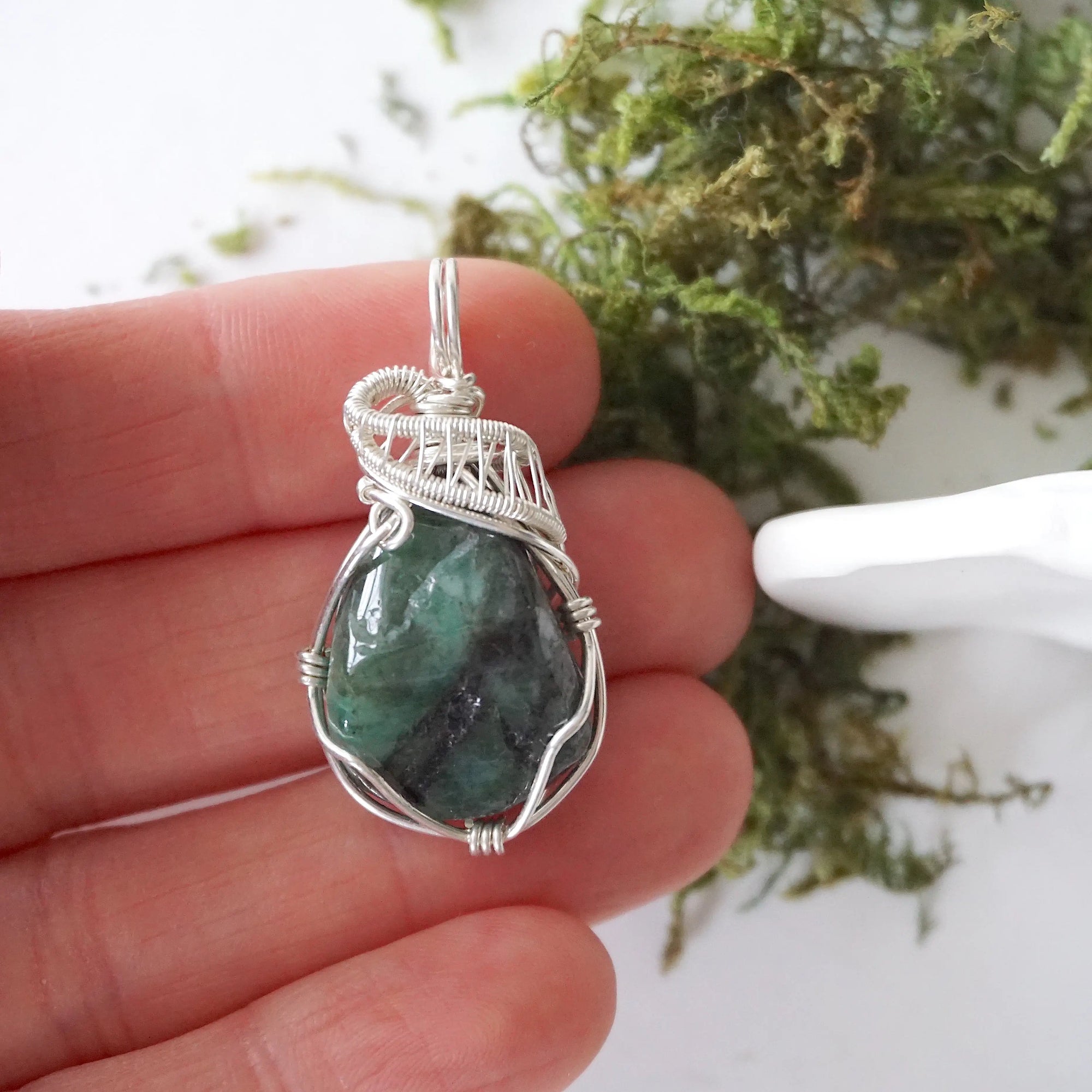 Polished raw emerald pendant necklace for women shown in hand for size reference with natural emerald and 925 sterling silver wire wrapping