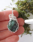 Polished raw emerald pendant necklace for women shown in hand for size reference with natural emerald and 925 sterling silver wire wrapping