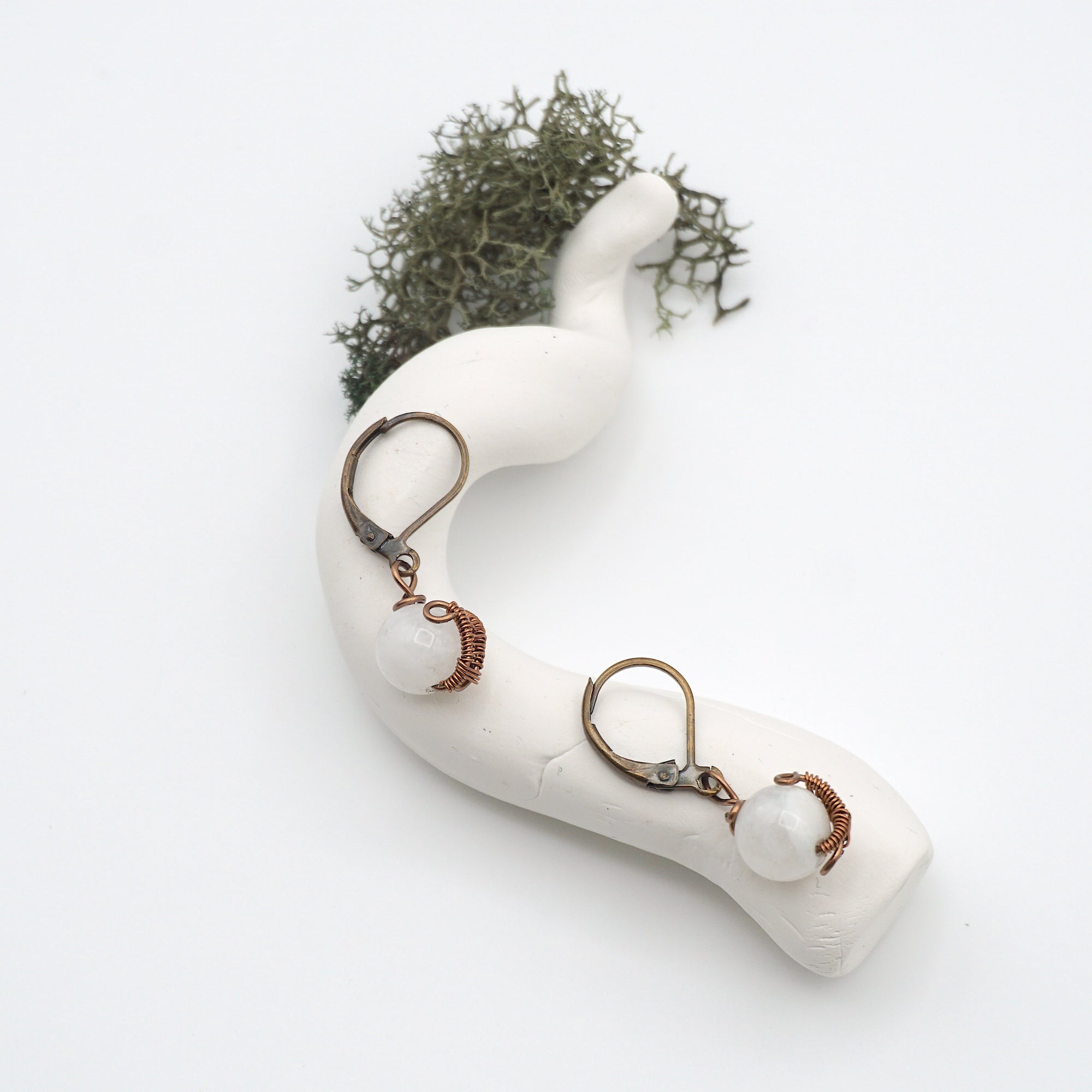 Bird’s eye view of rainbow moonstone drop earrings laying flat on a display, showing detailed wire wrapping and gemstone iridescence.