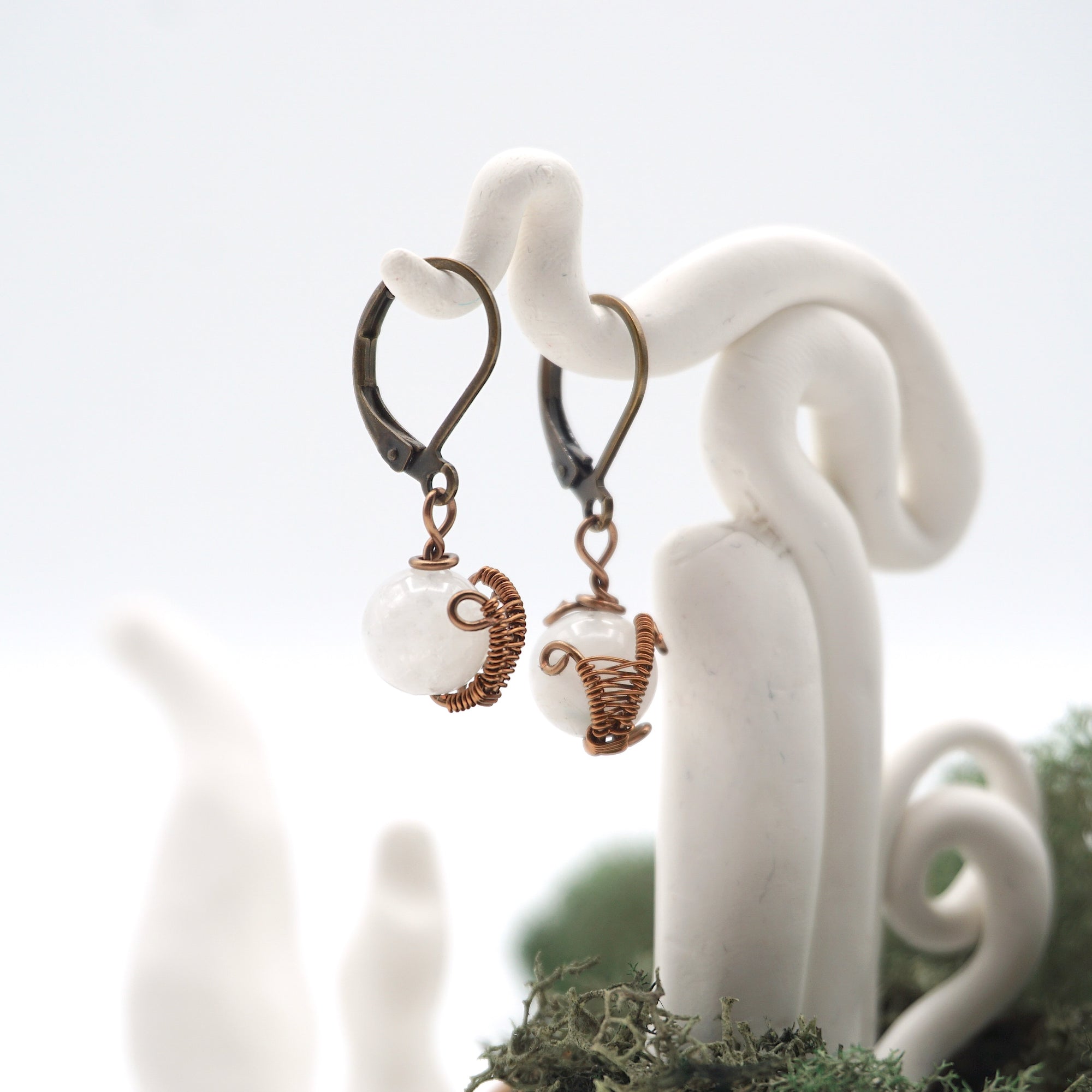 Side angle of rainbow moonstone drop earrings on a display stand, highlighting antique bronze copper wire wrapping.