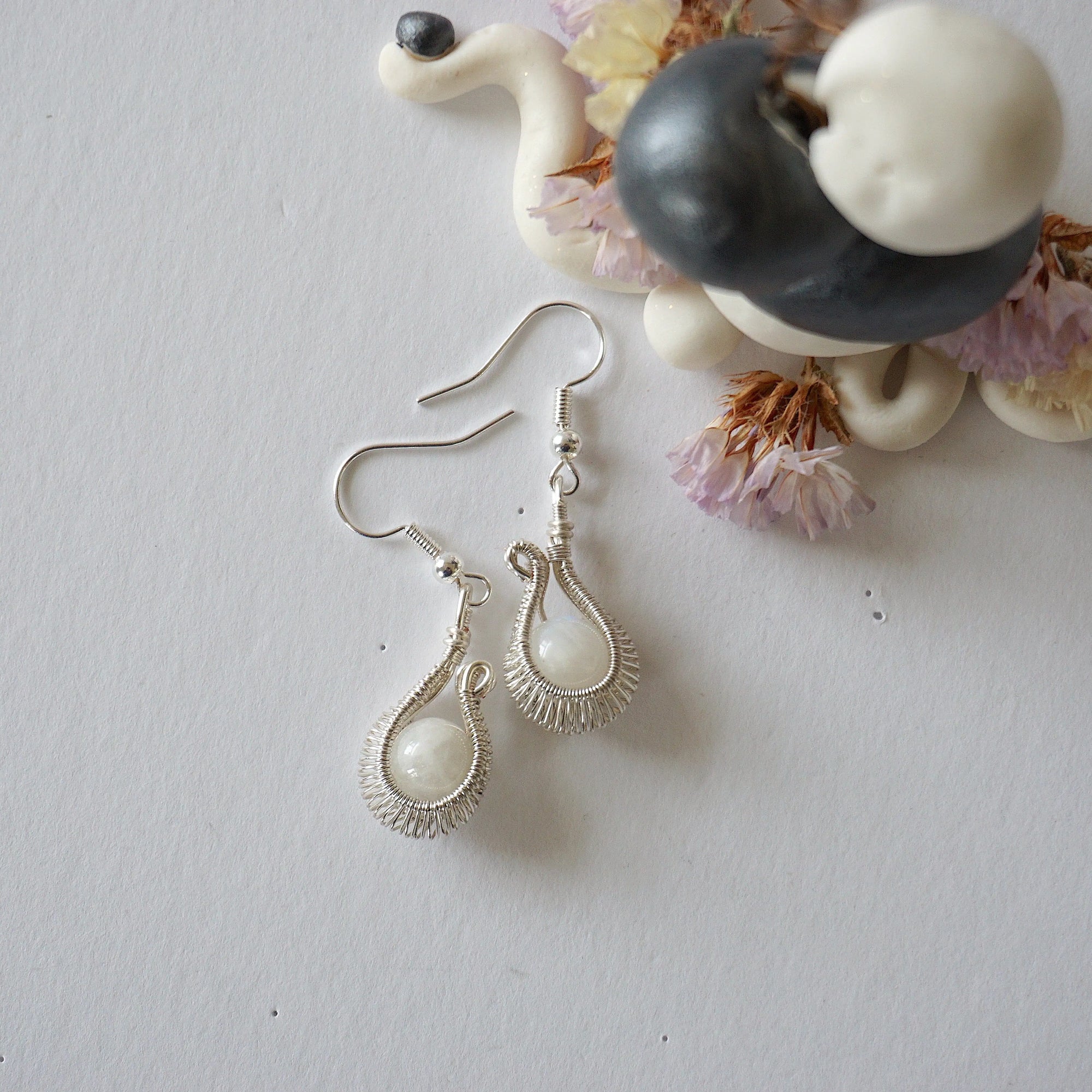Flat lay of rainbow moonstone drop earrings showing fish hook ear wire style and handcrafted soft silver wire wrapped moonstone beads.