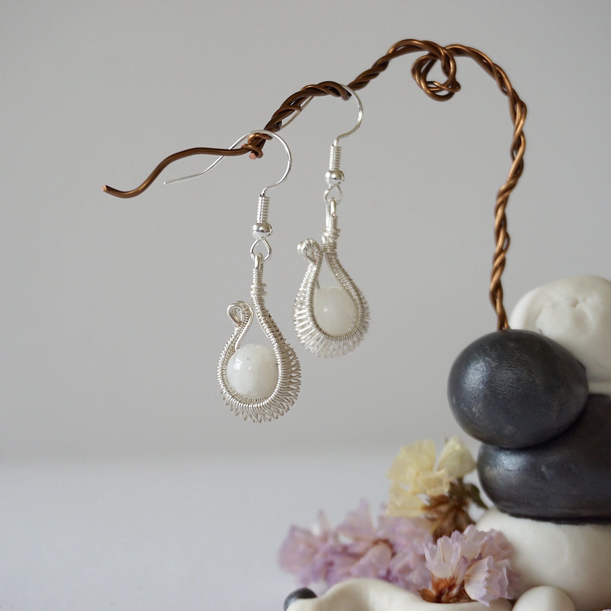 Macro close-up showing detailed artisan wire wrapping in soft silver copper around natural rainbow moonstone bead on drop earrings.