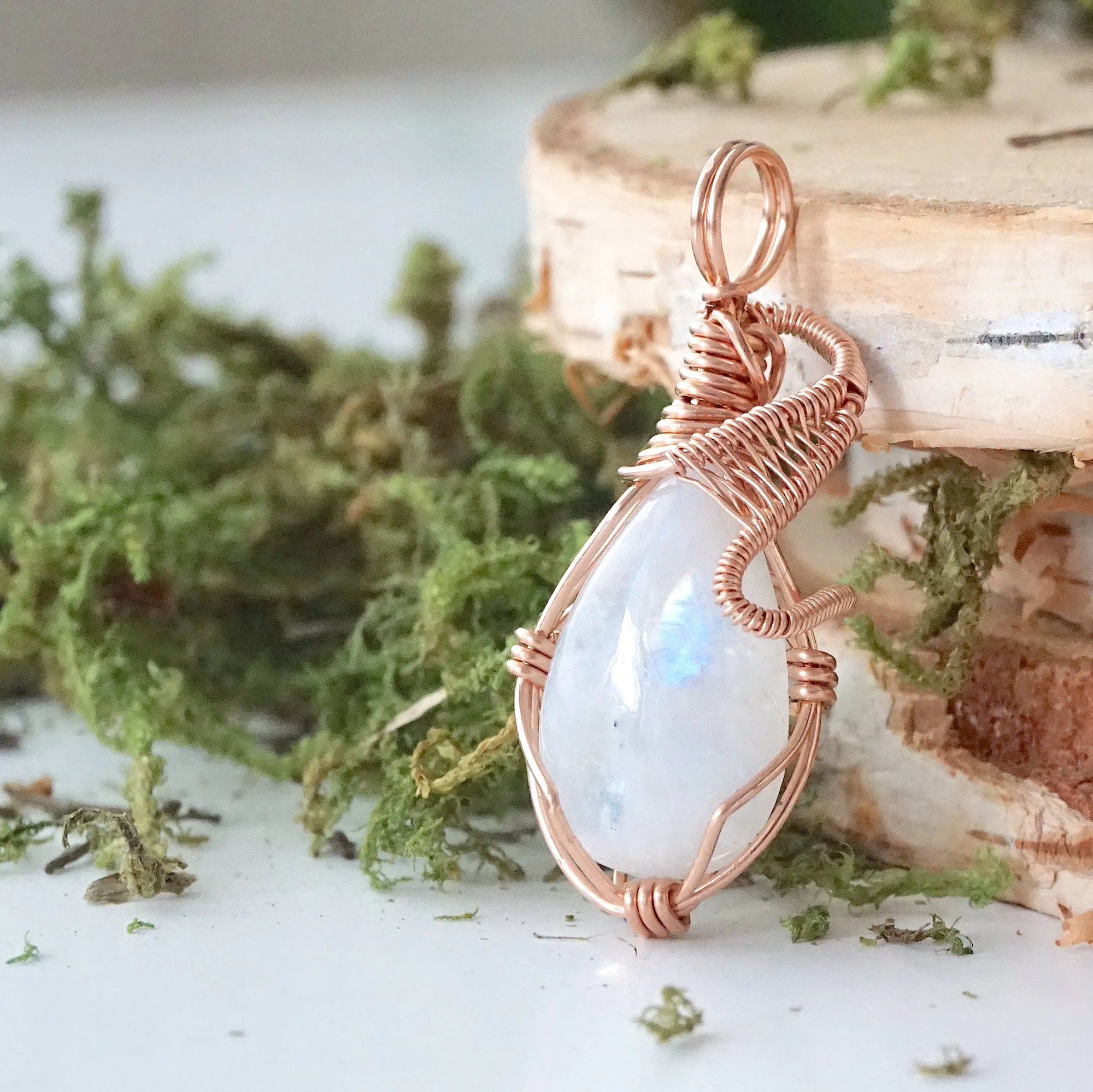Angled close-up of natural rainbow moonstone cabochon pendant with detailed 14k rose gold filled wire wrapping