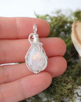 Rainbow moonstone pendant shown in hand for size reference with handcrafted 925 sterling silver wire wrap for women