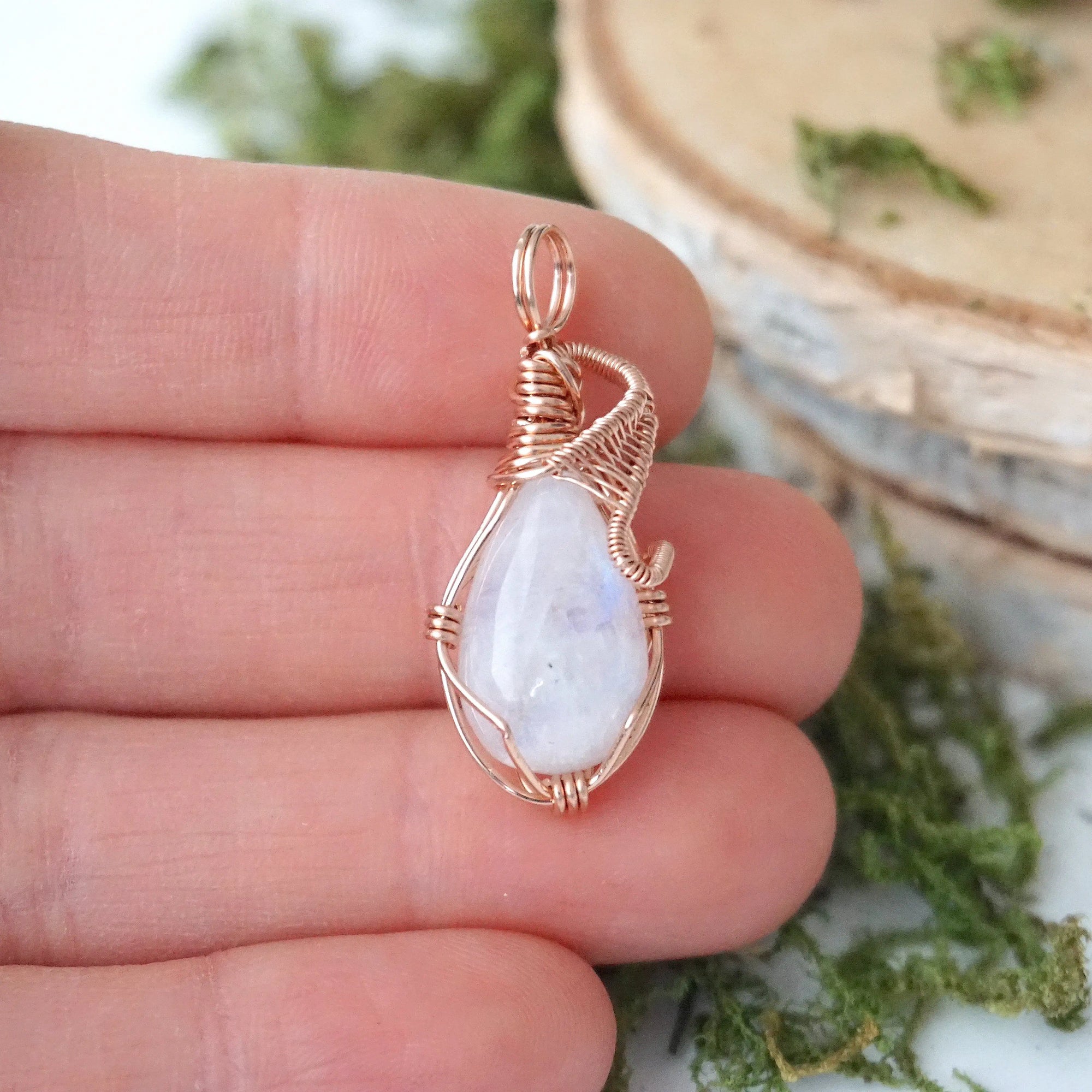 Rainbow moonstone cabochon pendant shown in hand for size reference with handcrafted 14k rose gold filled wire wrap