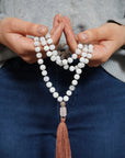 Rainbow moonstone mala necklace with 108 beads and rose quartz guru bead held in hands, knotted silk cord meditation necklace with brown tassel.