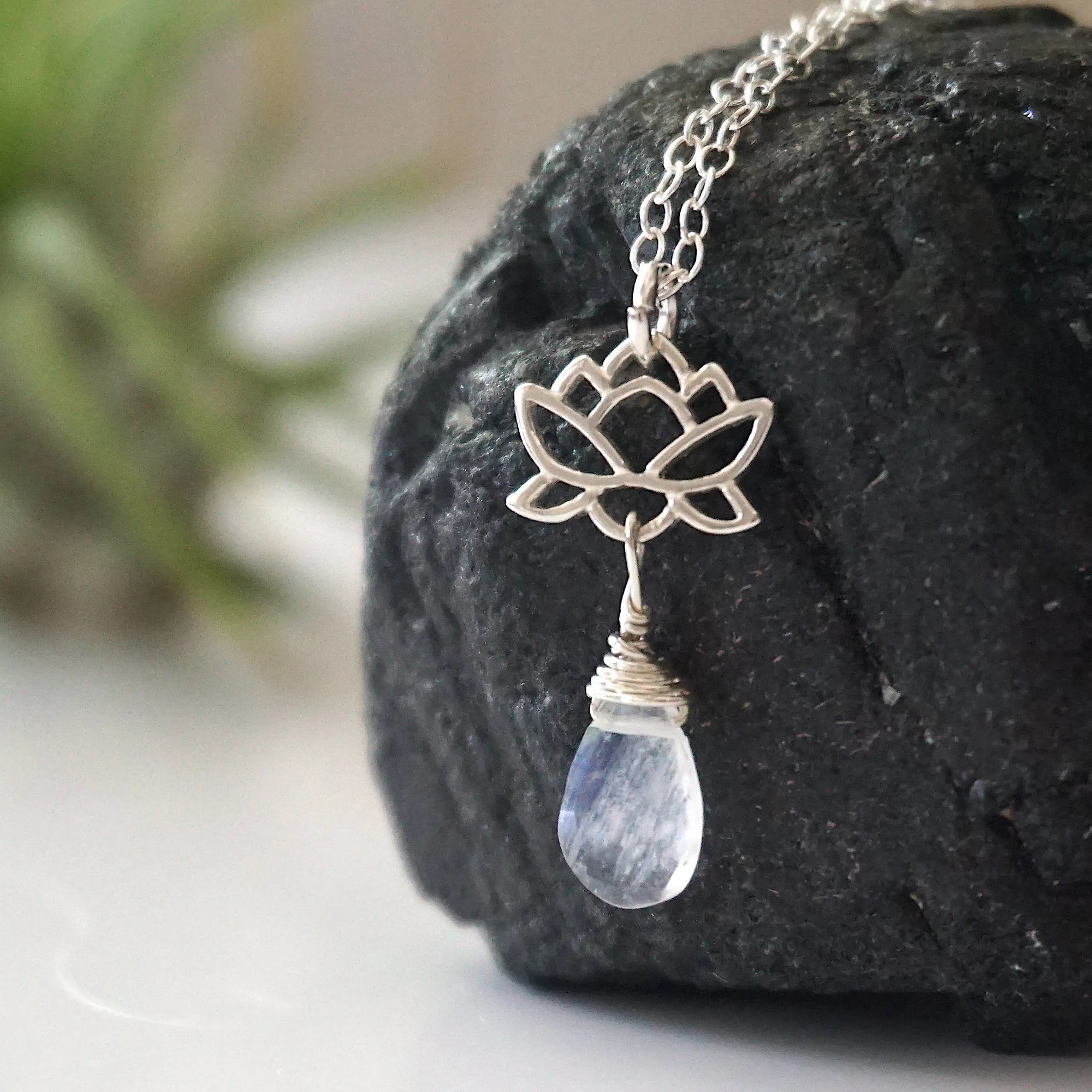 Left angle close-up highlighting handcrafted details of rainbow moonstone and lotus necklace, sterling silver lotus charm and faceted pear moonstone pendant.