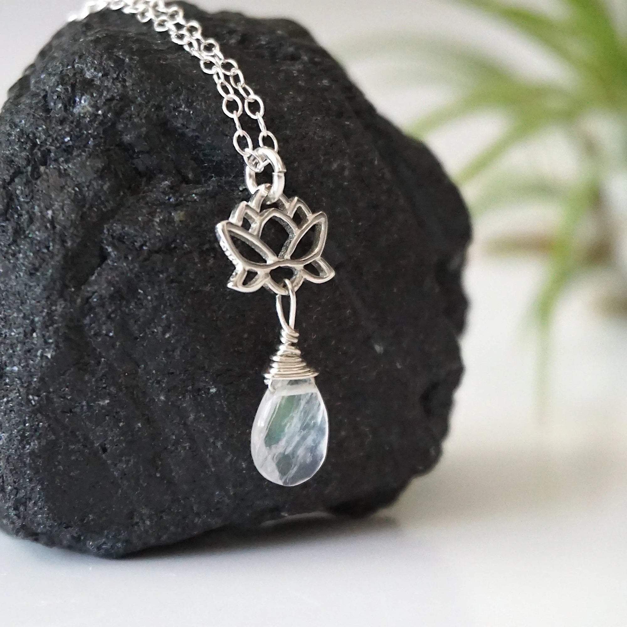 Right angle close-up showing artisan design of rainbow moonstone and lotus necklace, 925 sterling silver lotus charm with faceted pear rainbow moonstone drop.