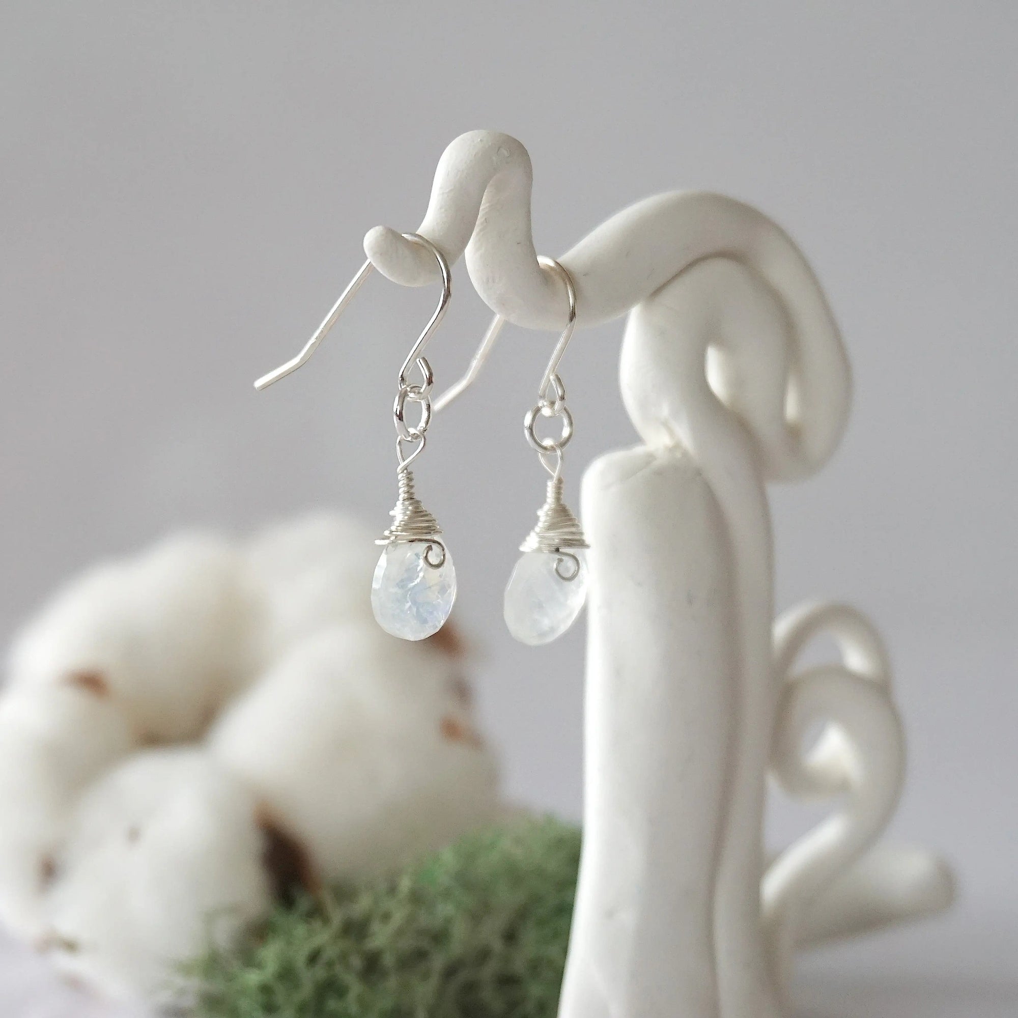 Side view of rainbow moonstone sterling silver drop earrings showing wire wrapped natural faceted rainbow moonstone, artisan craftsmanship, on a display – Designs by Nature Gems