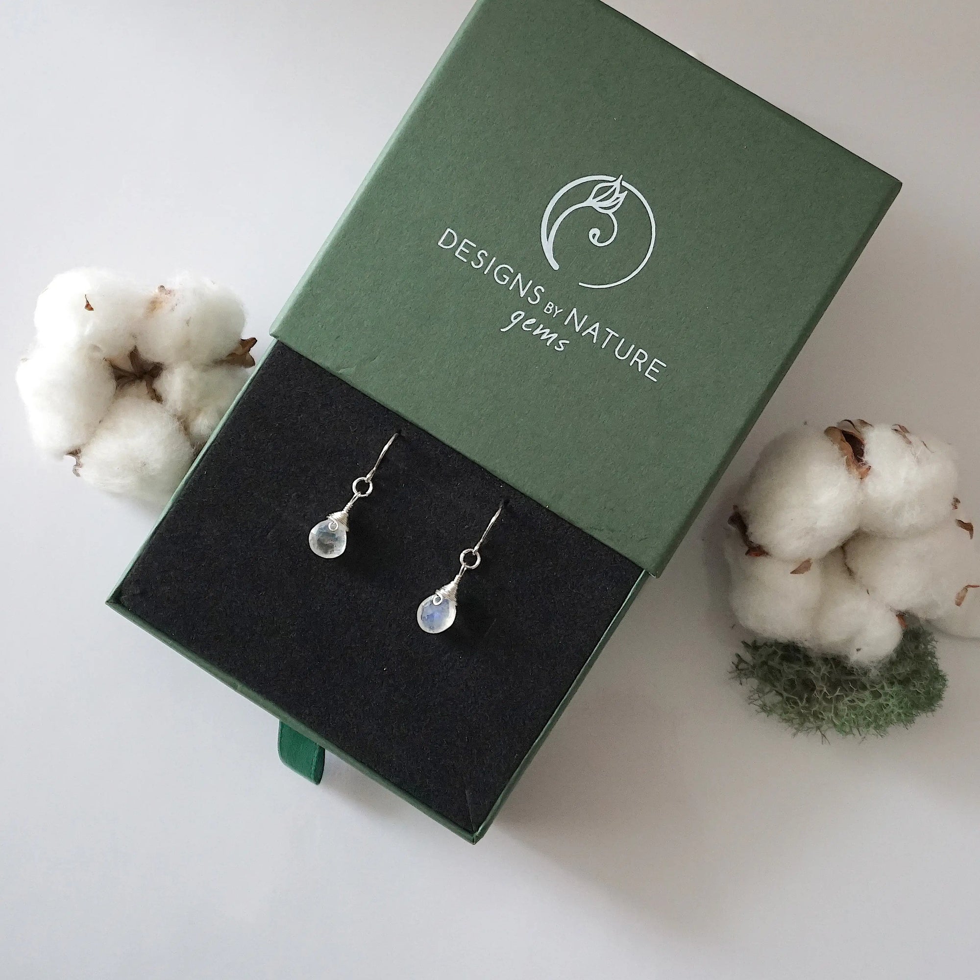 Rainbow moonstone sterling silver drop earrings in branded Designs by Nature Gems jewelry box, showcasing handcrafted faceted rainbow moonstone and sterling silver wire wrapping