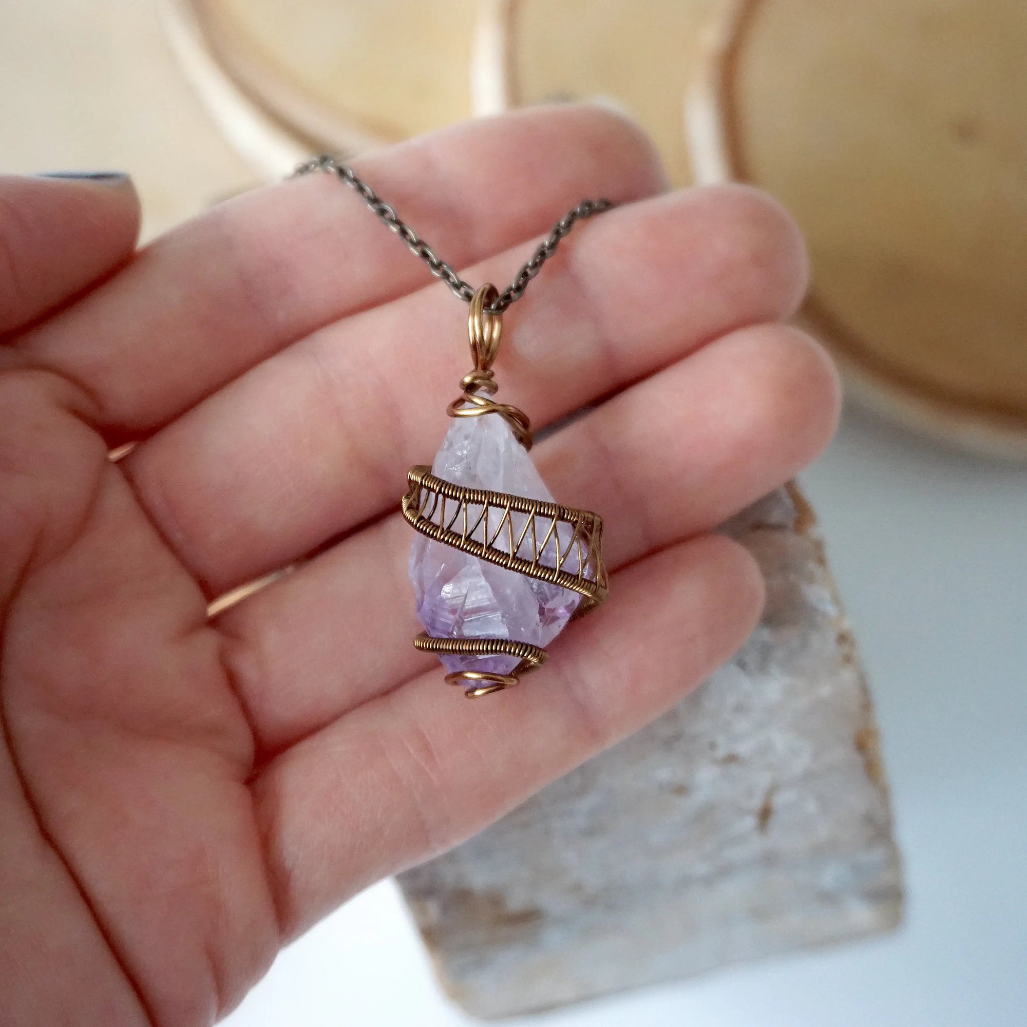 Raw amethyst point pendant necklace on antique bronze chain held in hand for size reference
