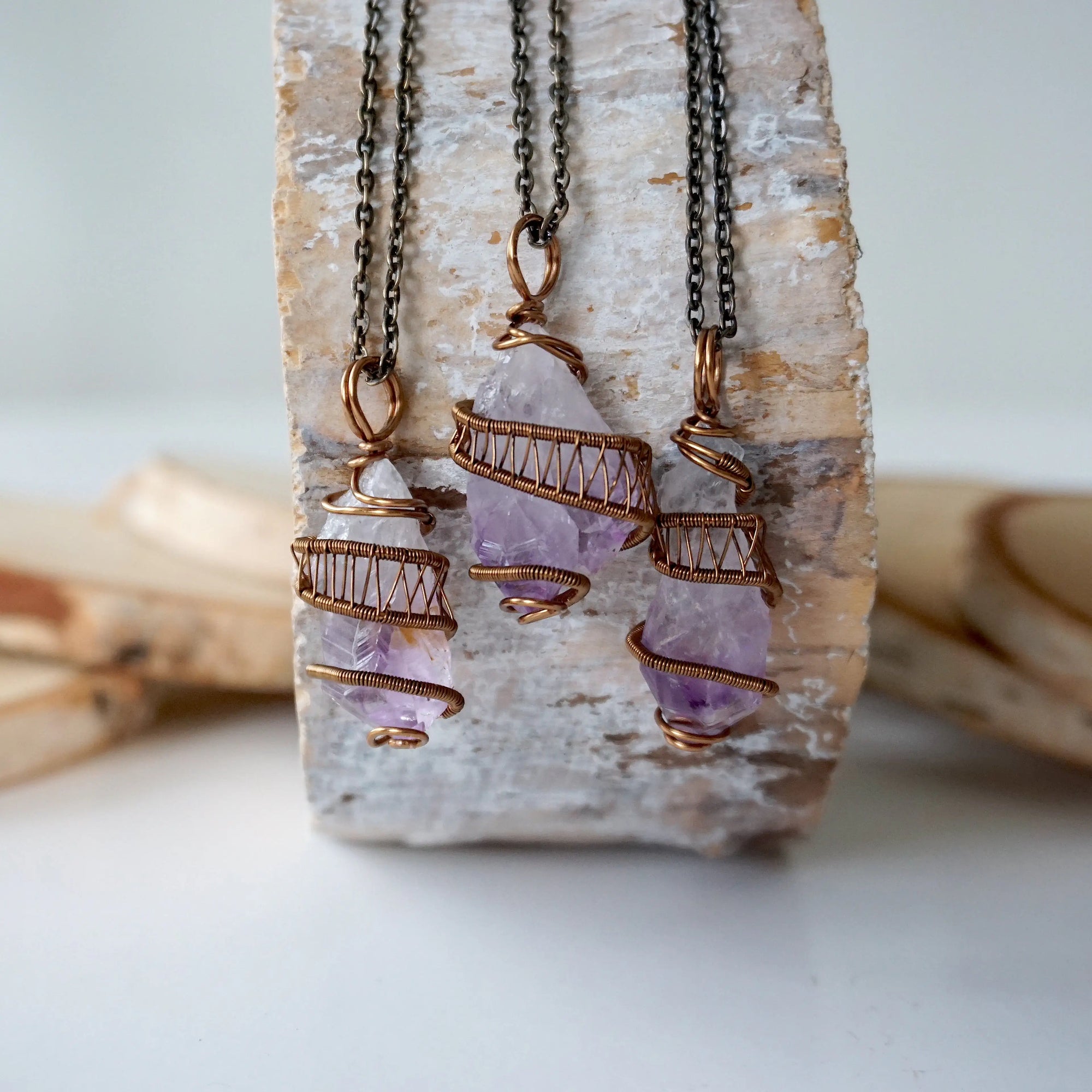 Three raw amethyst point pendant necklaces on antique bronze chain showing natural variation in crystal color, size, and shape