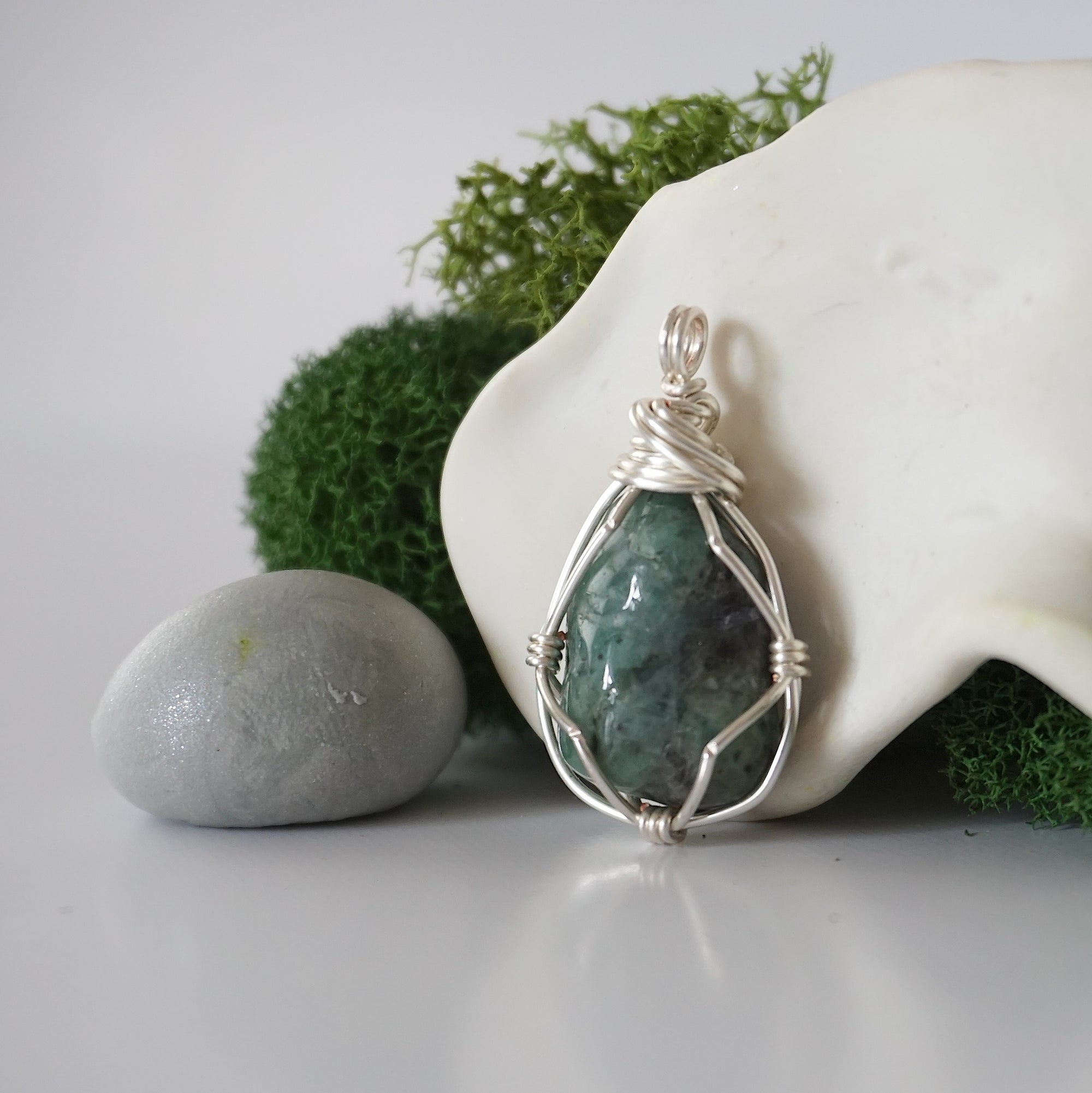 Detailed side angle view of simple raw emerald pendant in silver wire