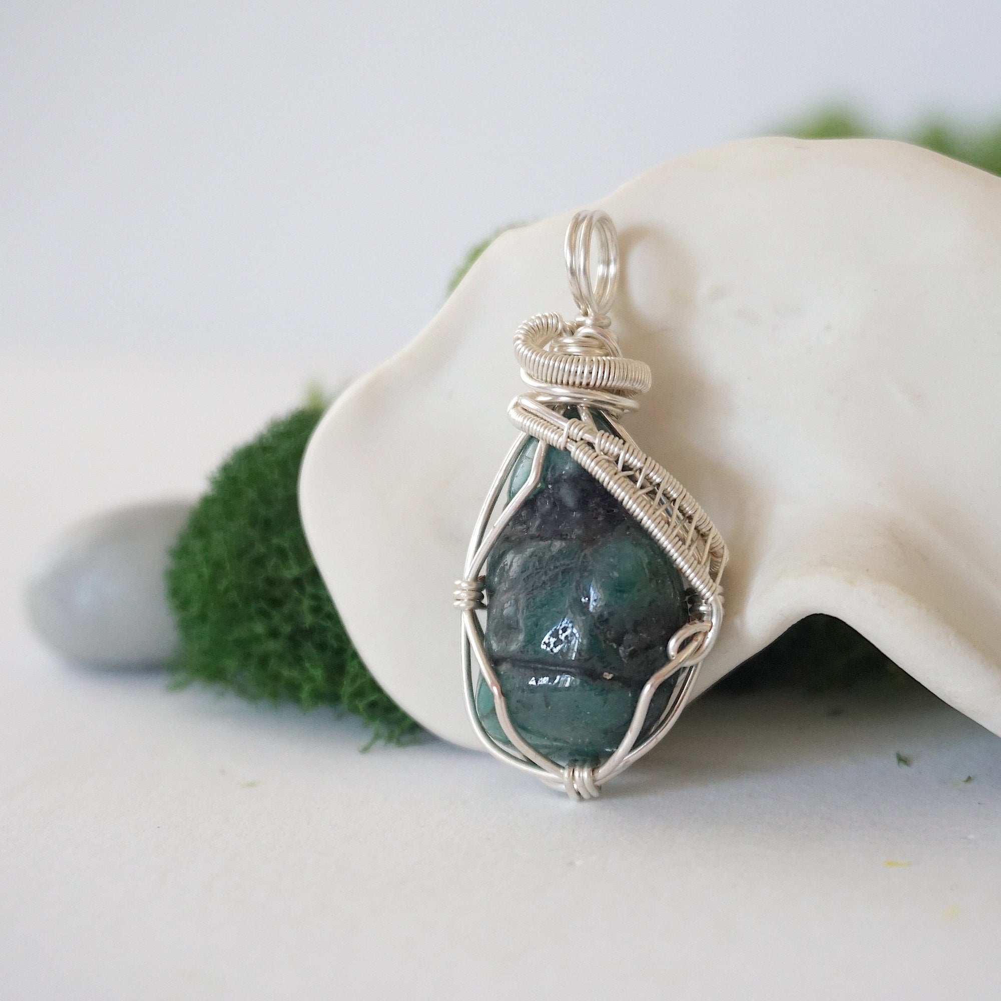 Side angle detail of natural emerald pendant highlighting intricate artisan wrapping in soft silver copper wire.