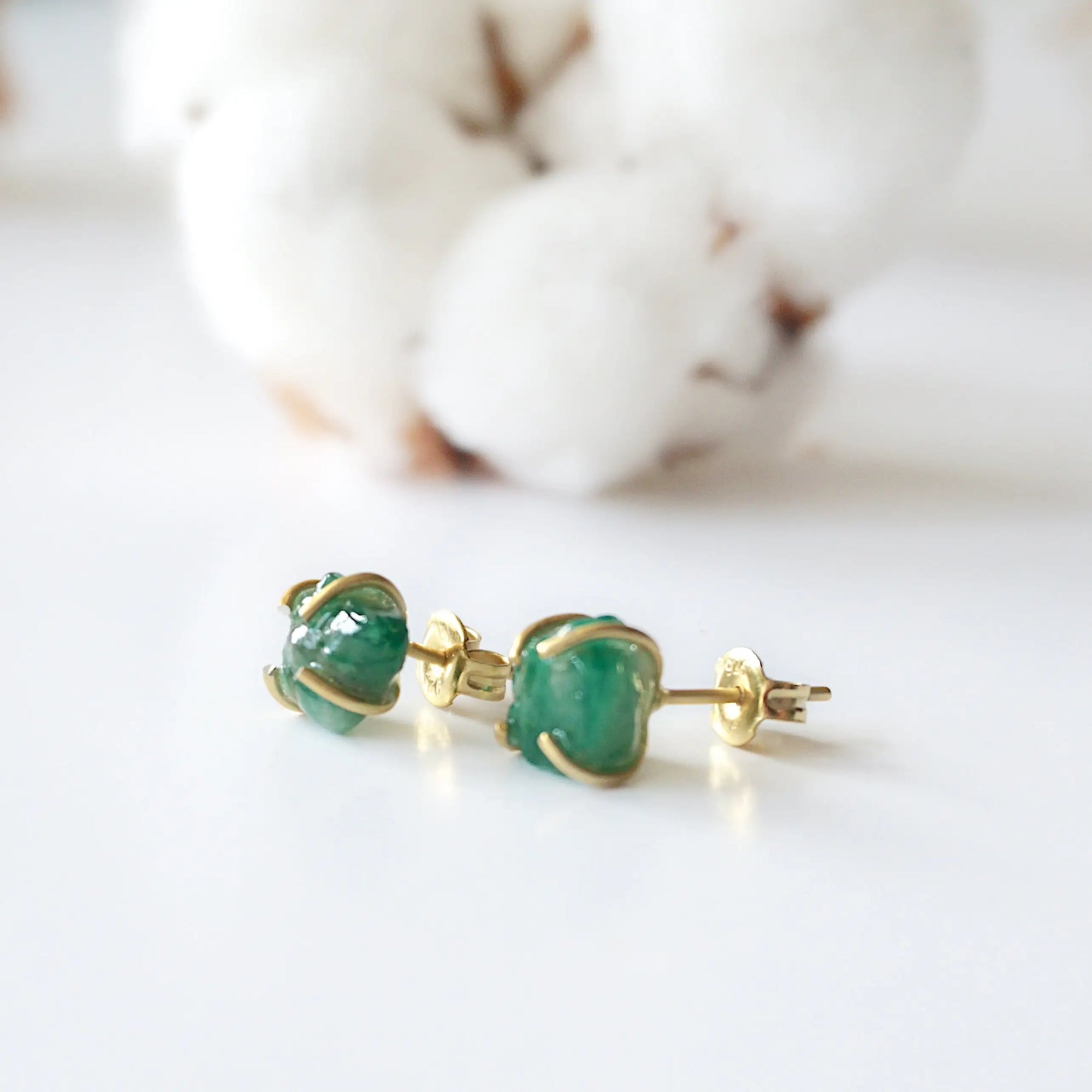Raw emerald stud earrings in 14k gold vermeil at a slight angle showing natural green emerald and minimalist prong setting