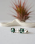 Raw emerald stud earrings in sterling silver at a slight angle showing natural green emerald and minimalist prong setting