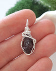 Raw garnet crystal pendant wire wrapped in sterling silver held in hand showing size