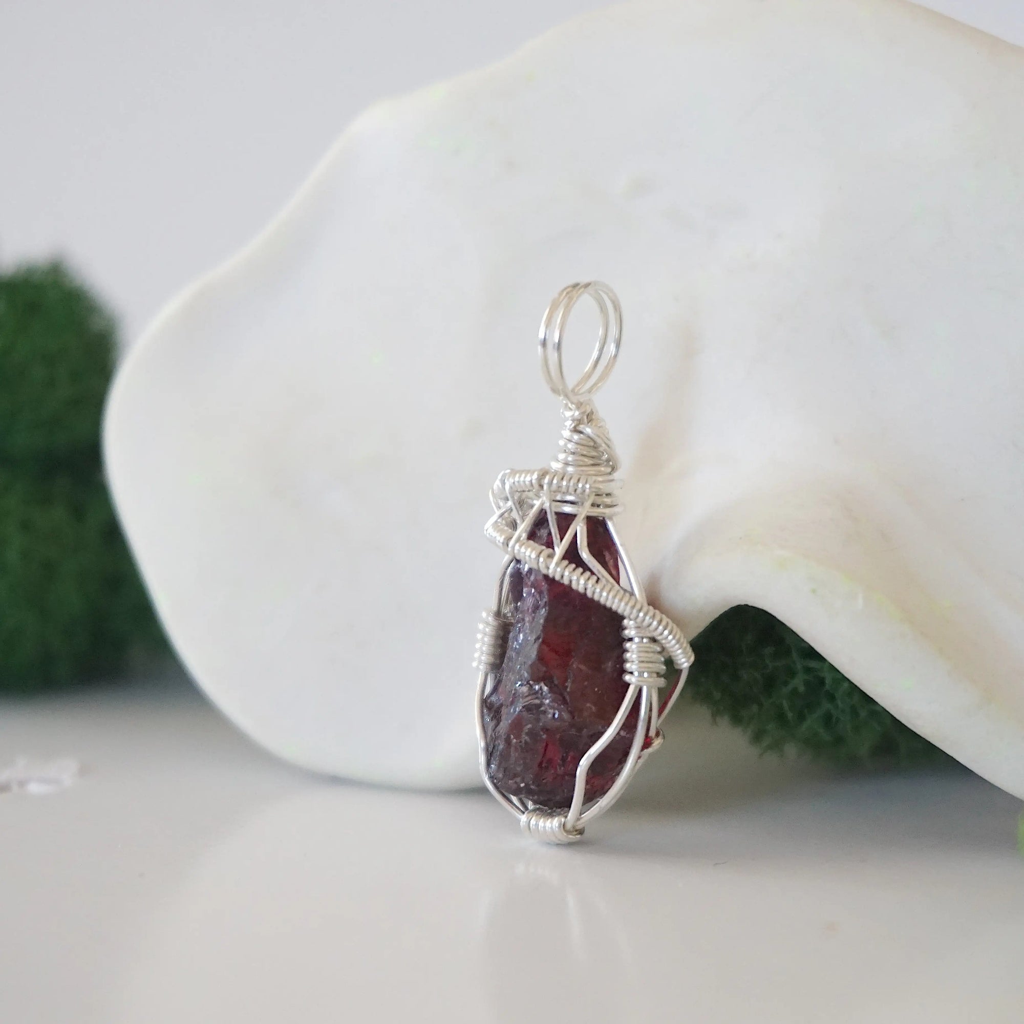 Side angle of raw garnet pendant showing artisan wire wrapped sterling silver detail