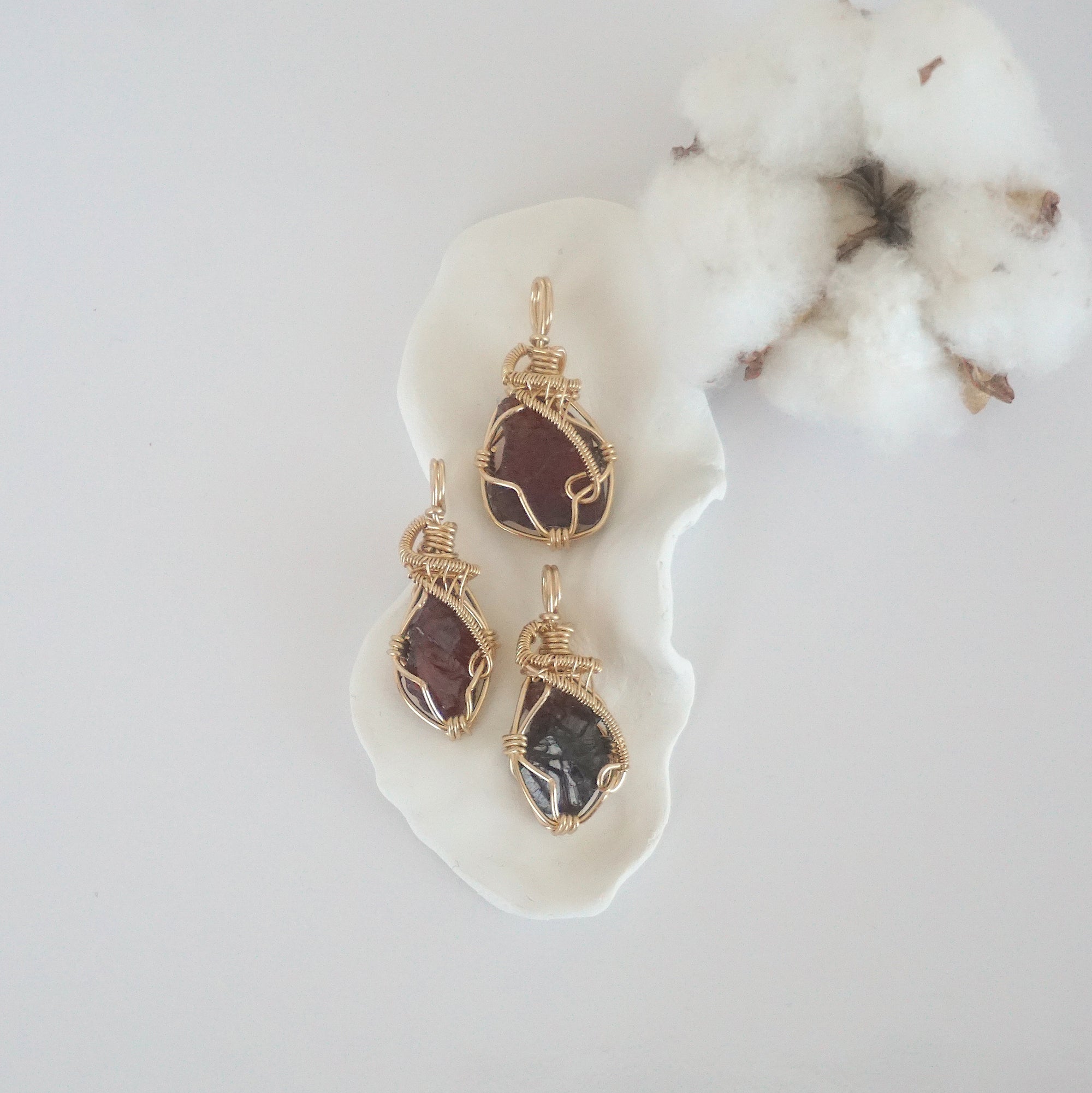 Three raw garnet pendants in 14k gold filled, showing natural variation in size, shape, and color. Handcrafted January birthstone jewelry by Designs by Nature Gems.