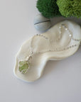 Simple raw peridot necklace with silver plated brass chain laying flat