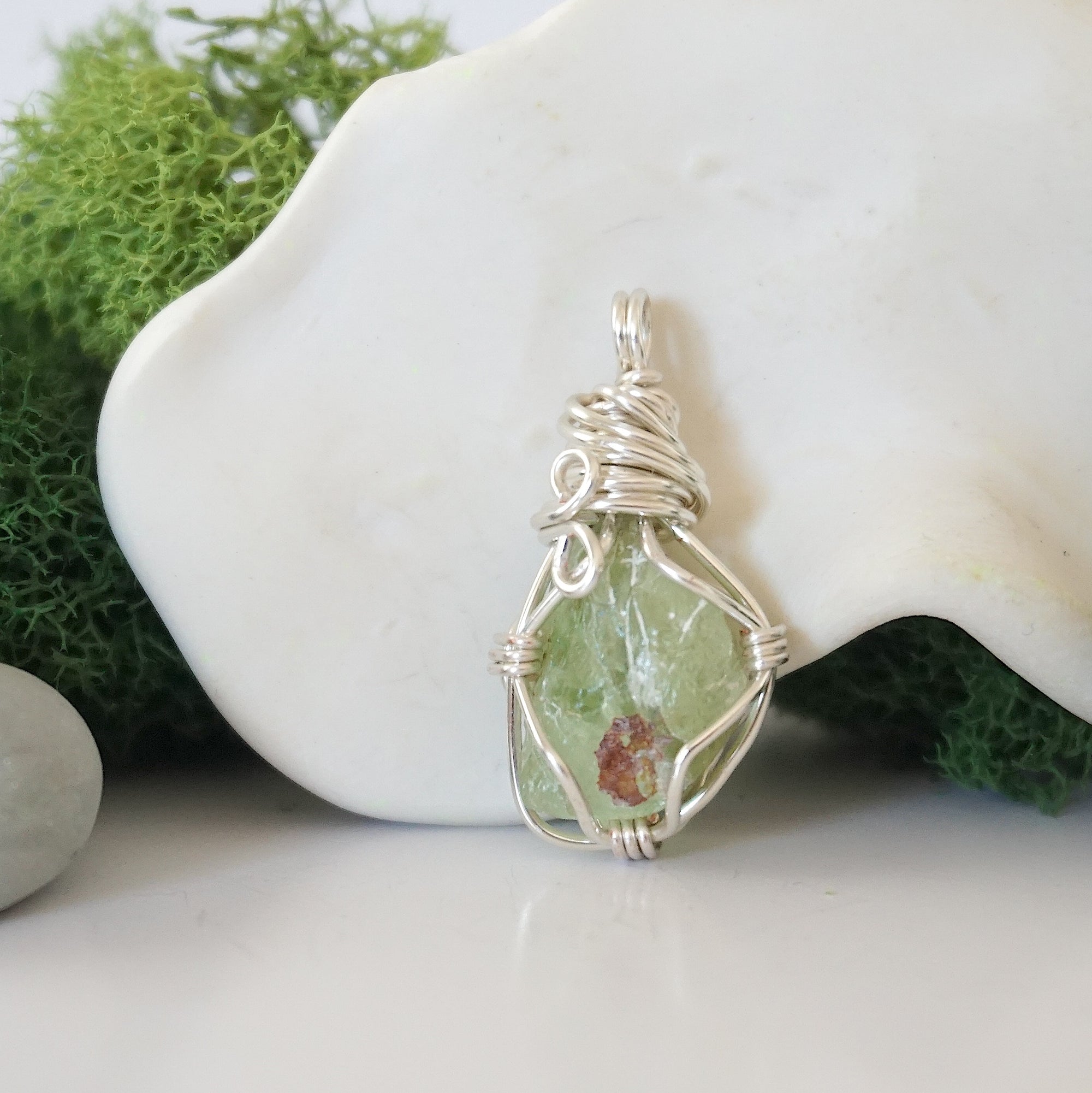 Back angle look at simple raw peridot pendant with silver wire wrapping