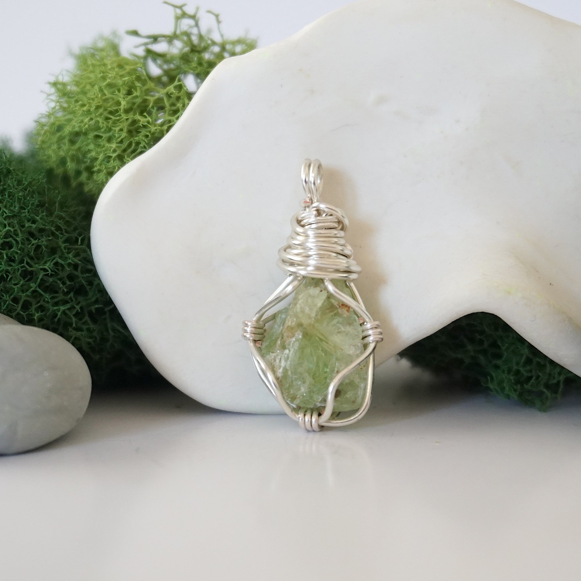 Detailed front angle view of simple raw peridot pendant in silver wire