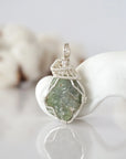 Front view of raw peridot pendant — natural unpolished green peridot stone hand-wrapped in detailed silver finish wire, handcrafted artisan crystal jewelry